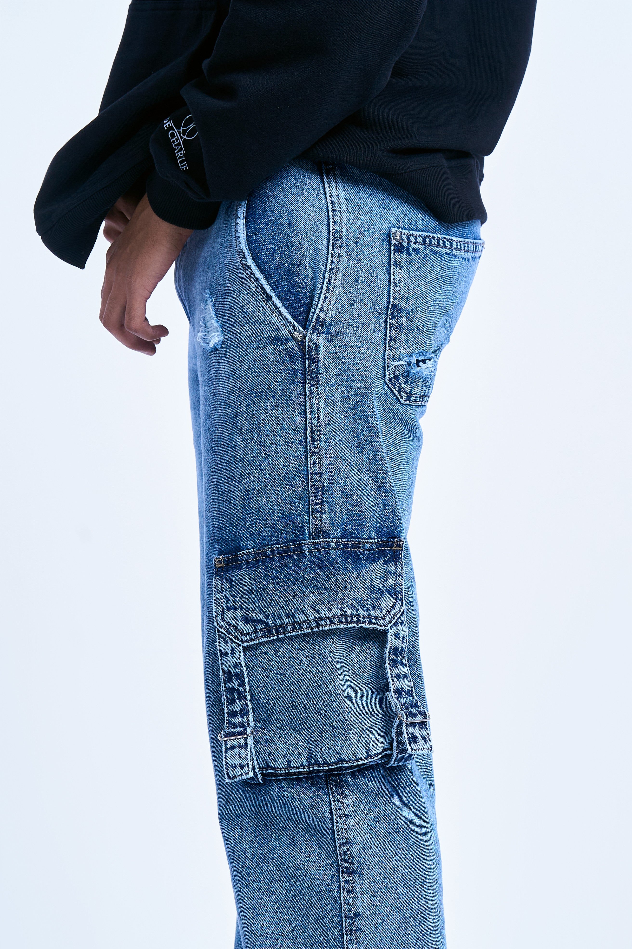MOE CHARLIE Ice Cargo Jeans 3/4-Seitenansicht – helle Waschung, Cargotasche mit Nieten, schwarze Sneakers