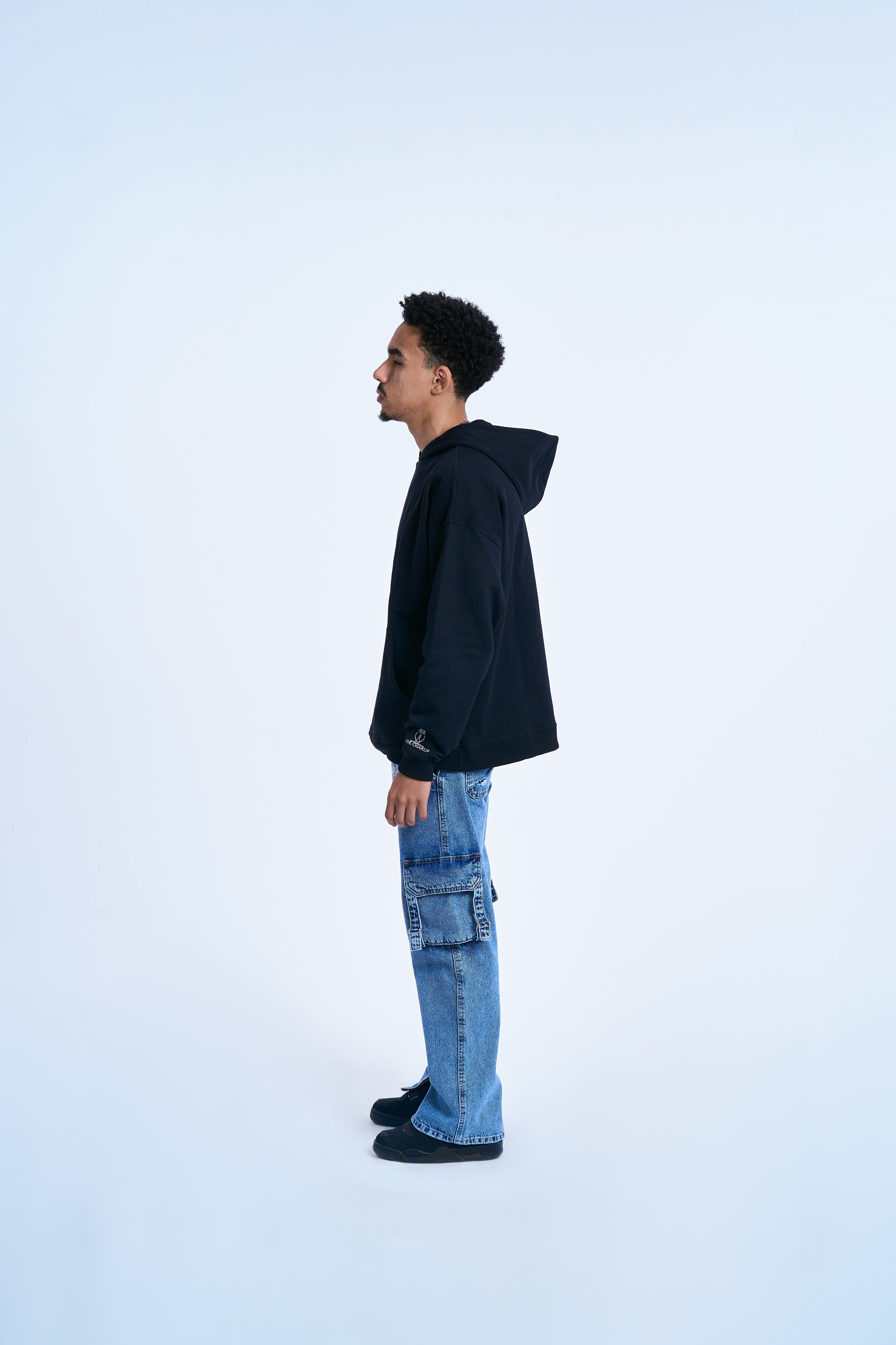 MOE CHARLIE Hoodie Schwarz, linke Seitenansicht maennlich, Sleeve-Logo am Aermelrand, Oversize-Passform