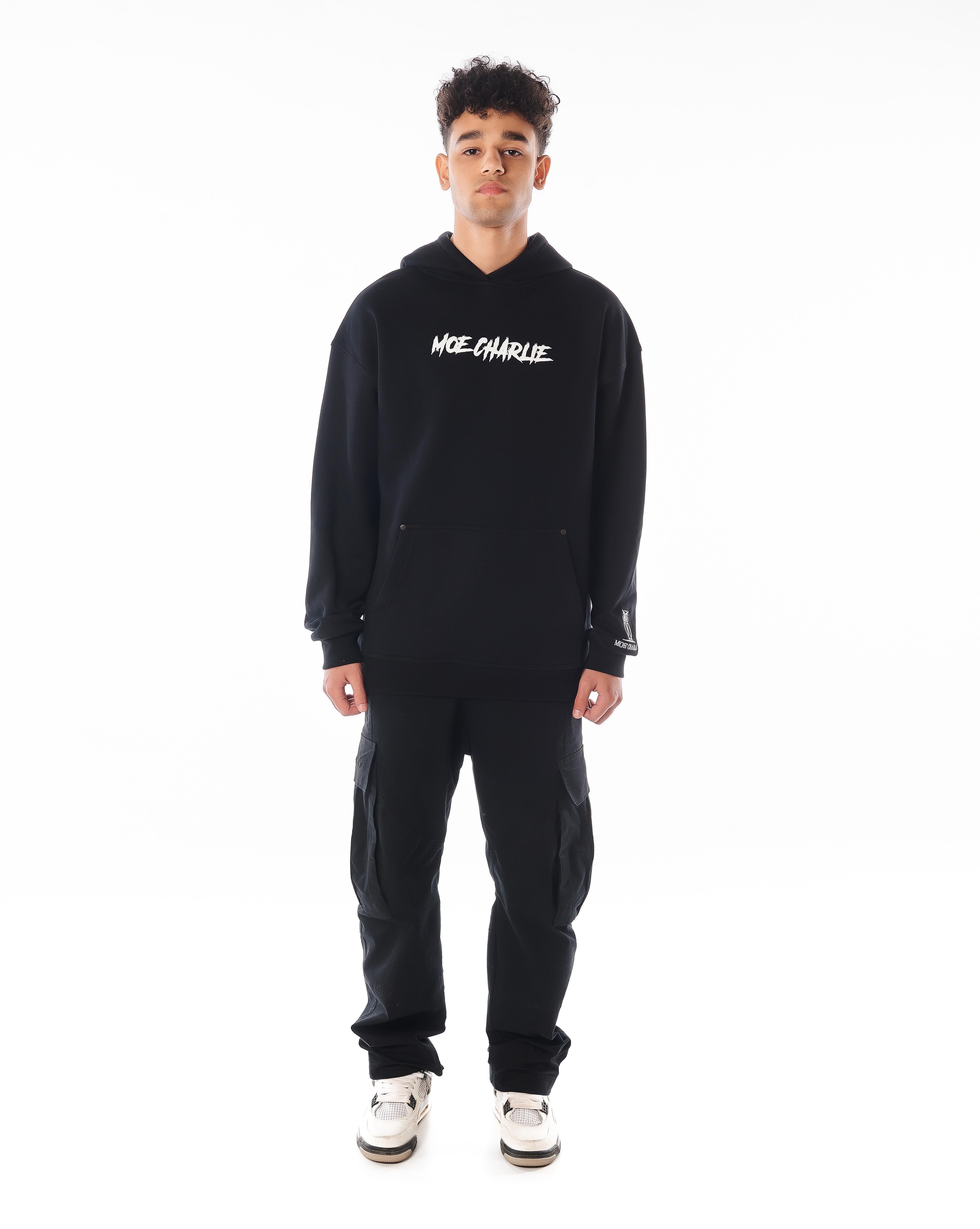 Frontansicht MOE CHARLIE Predator Hoodie in Schwarz, Puff-Print Brust, Eulen-Logo am Ärmelabschluss, Cargo-Hose