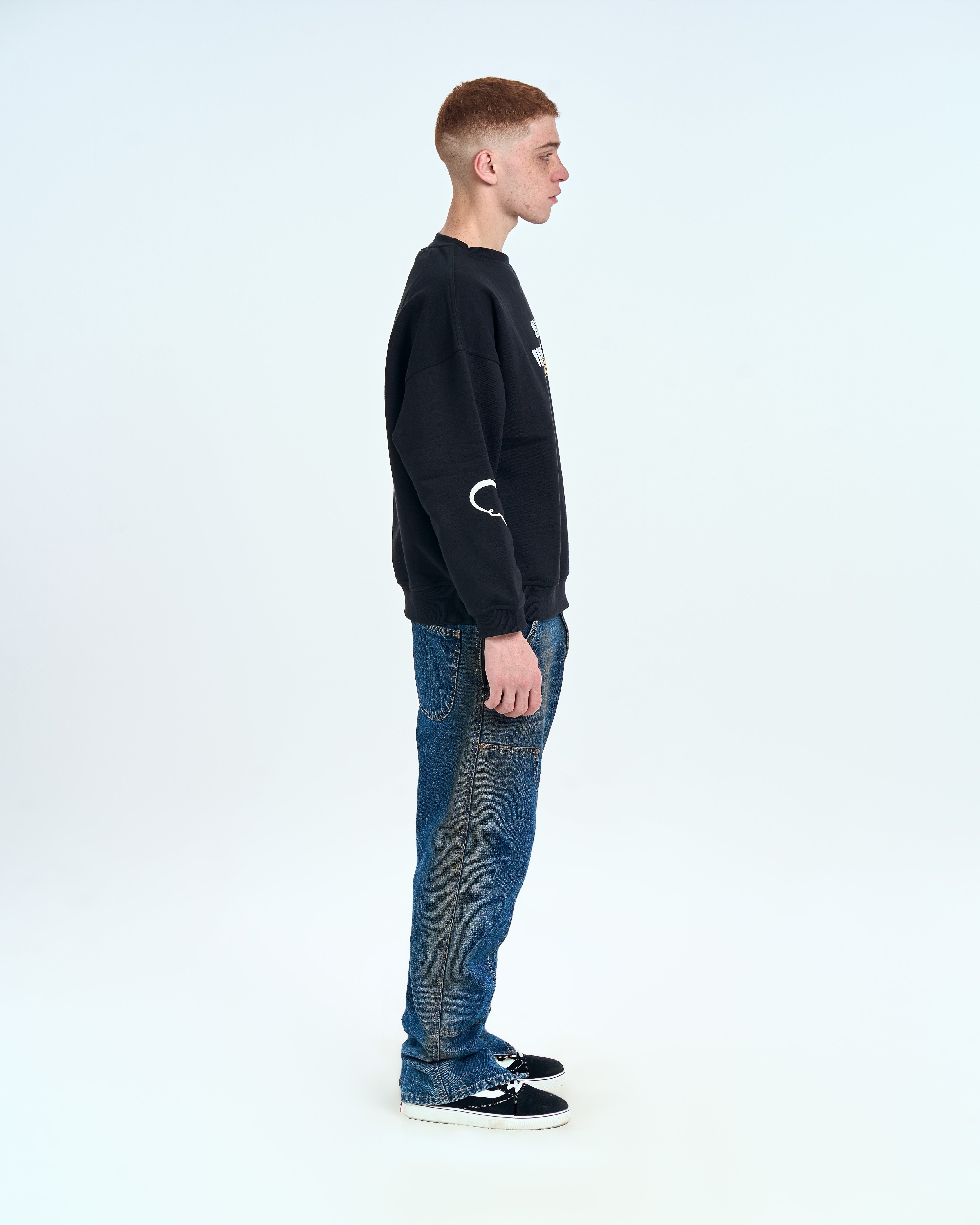 MOE CHARLIE Forbidden Sweater Schwarz - Seitenansicht links, Herz-Grafik am Ärmel, blaue Carpenter-Jeans
