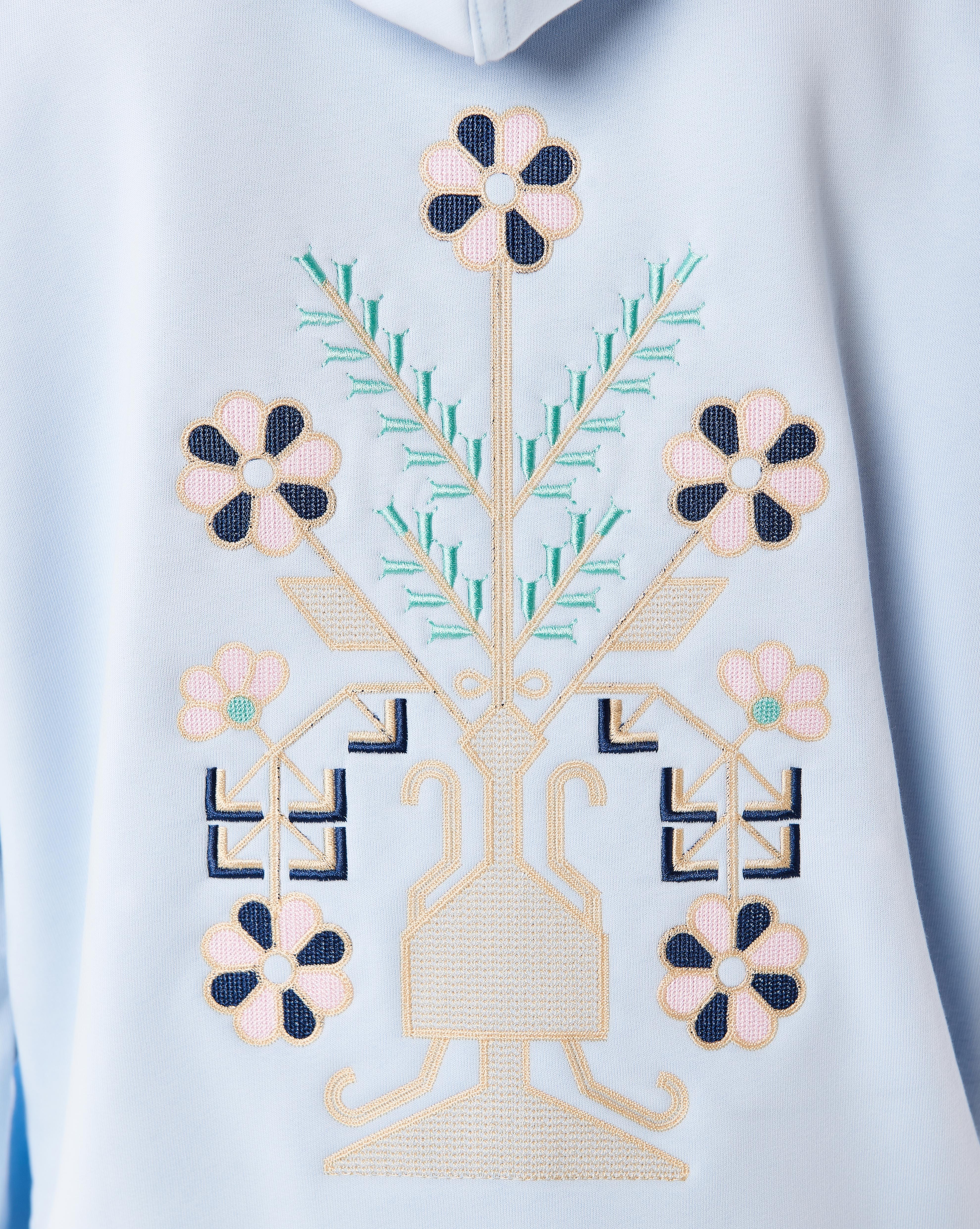 Makroaufnahme der großen Rücken-Stickerei des MOE CHARLIE Culture Hoodies, Vasenmotiv mit Blüten in Blau und Beige