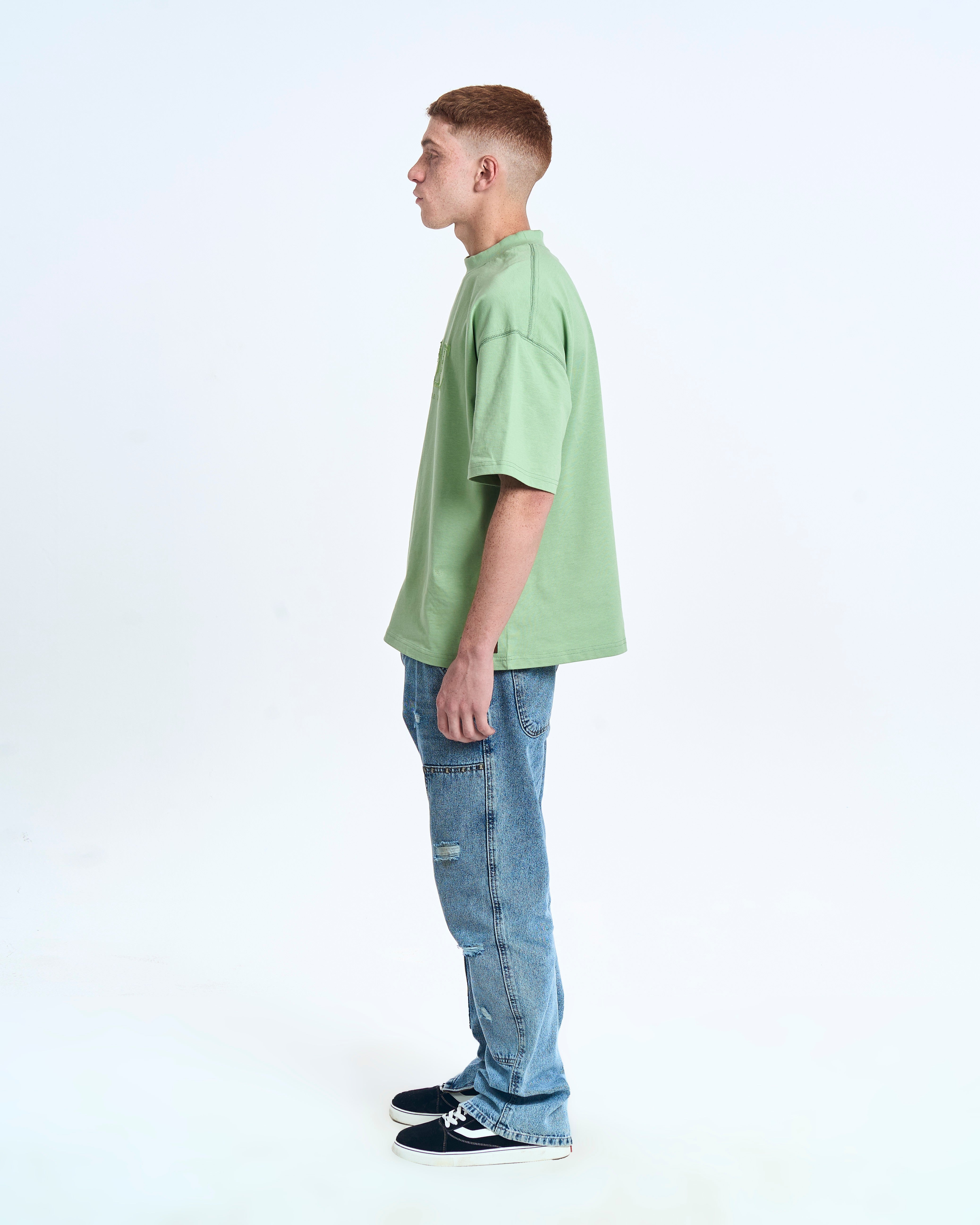 MOE CHARLIE Born In Exile T-Shirt Mintgrün – Seitenansicht rechts, Oversize-Silhouette, blaue Distressed-Jeans