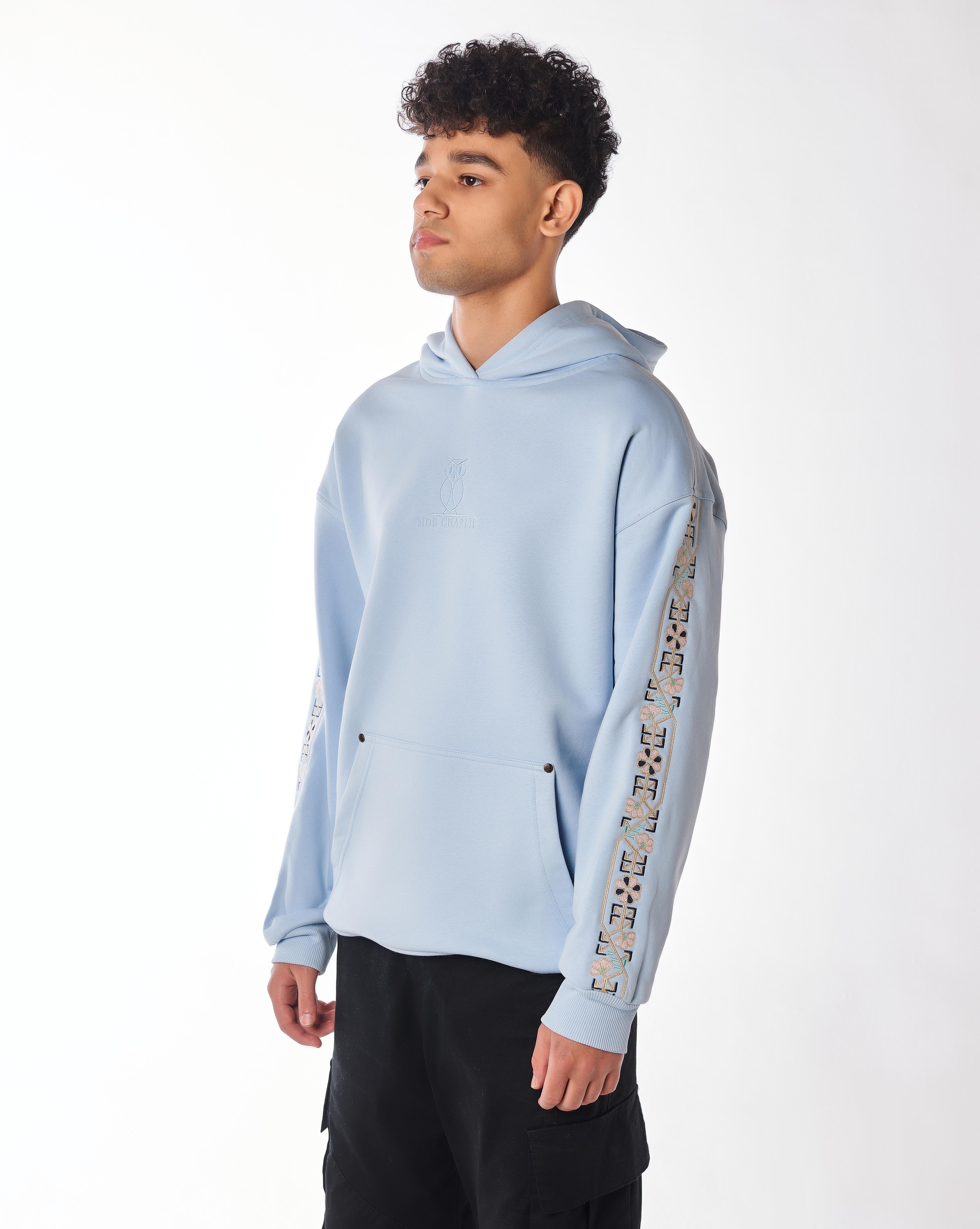 The Culture Hoodie in Riviera Blue, seitliche Dreiviertelansicht, ornamentale Blumenstickerei am Ärmel gut sichtbar