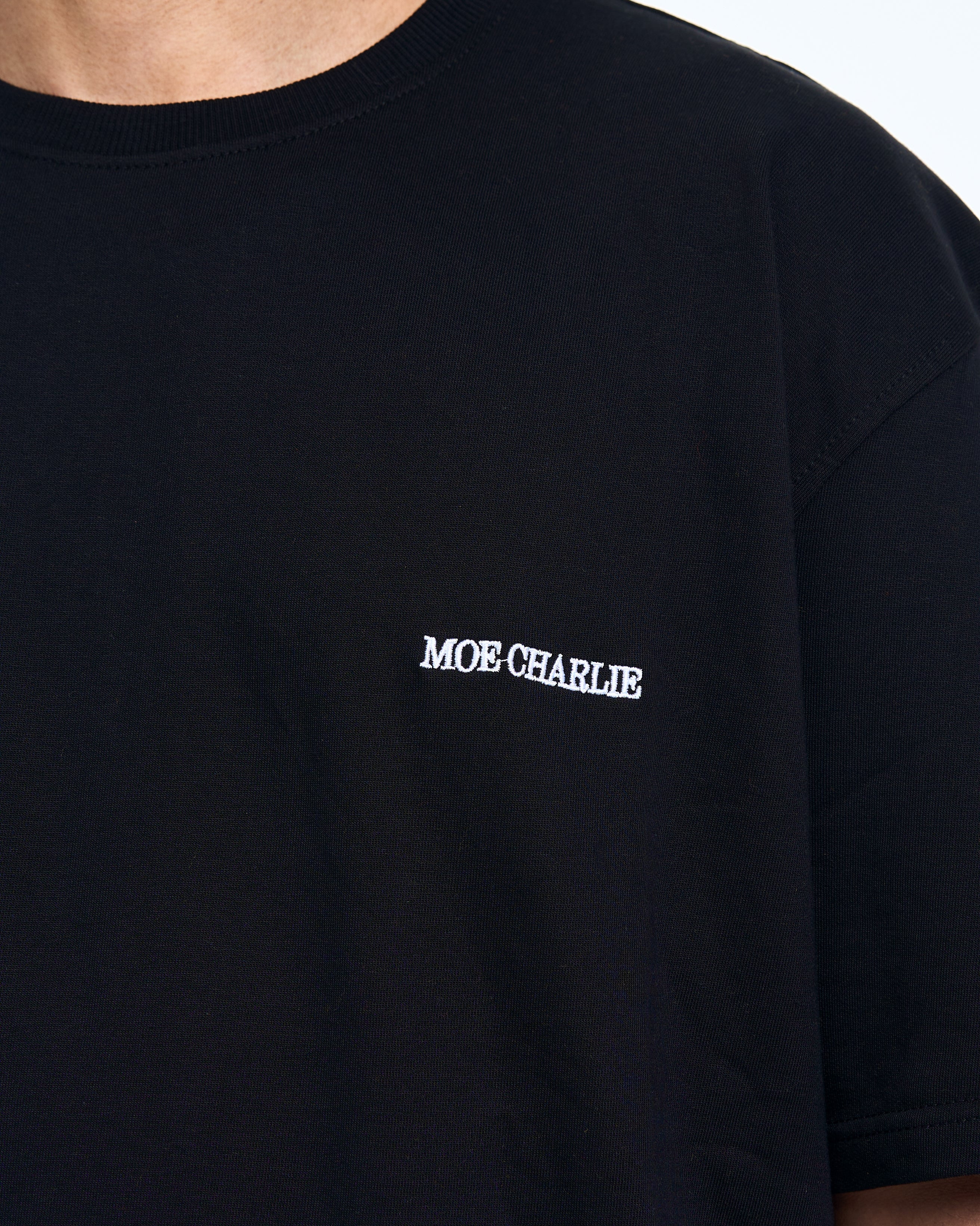 Detailaufnahme Brust-Stickerei – weißes MOE CHARLIE Schrift-Logo auf schwarzem Oversize-Shirt, Nahaufnahme