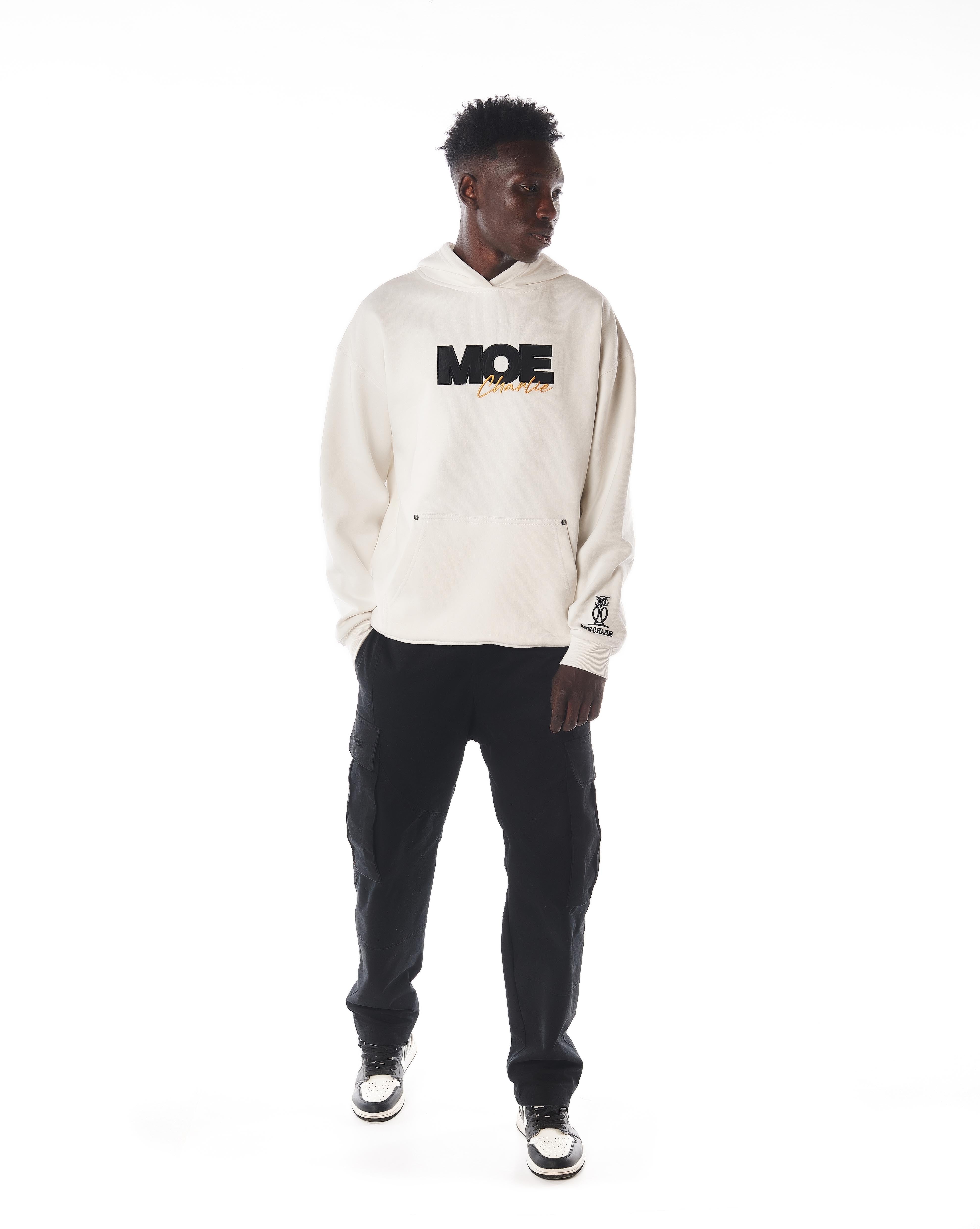 Dreiviertelansicht links MOE CHARLIE Gold Passion Hoodie, Frontprint seitlich, Jordan 1 Sneakers sichtbar