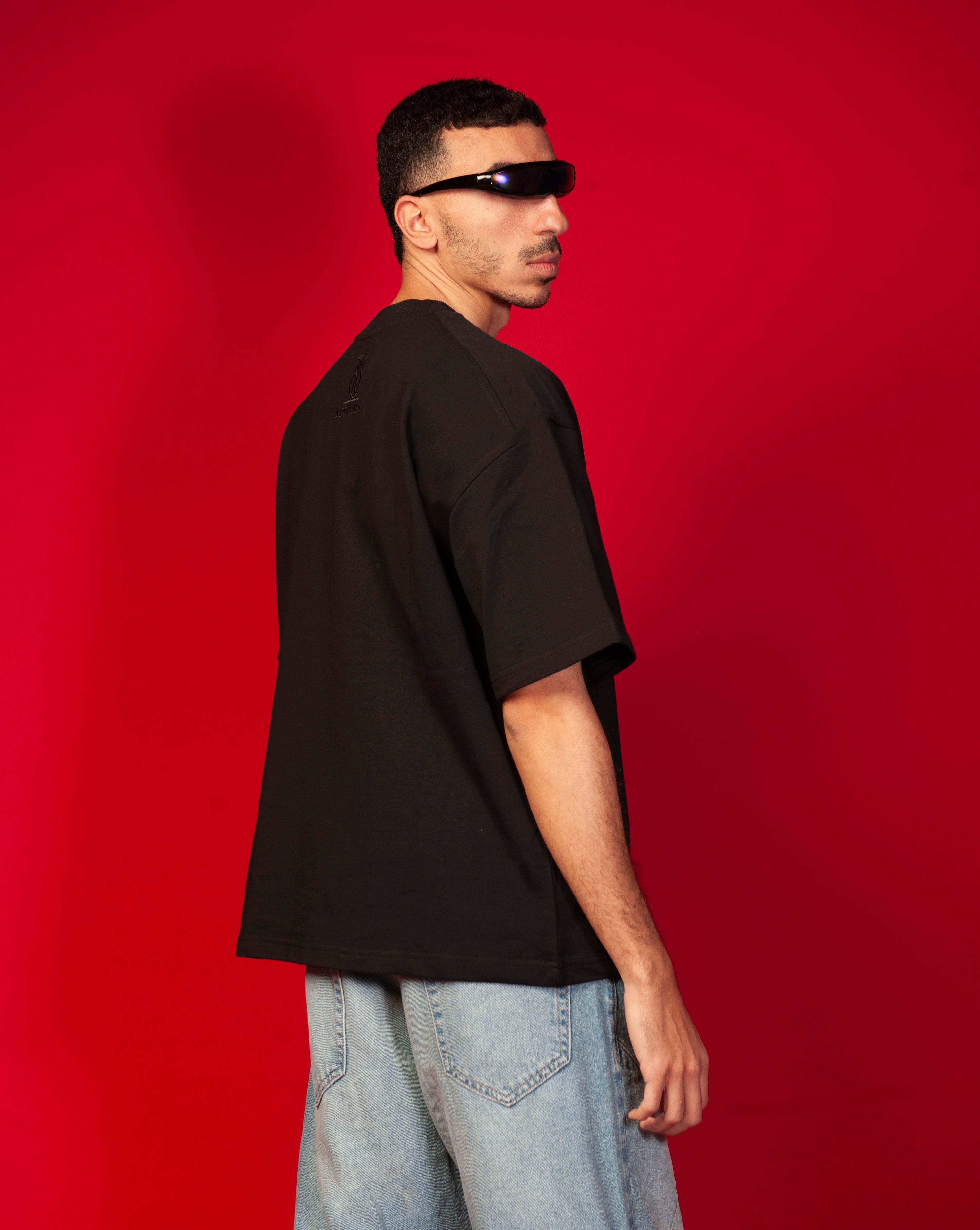 Genius T-Shirt MOE CHARLIE Seiten-Rueckenansicht, maennlich blickt zurueck, saubere schwarze Rueckseite, blauer Visor