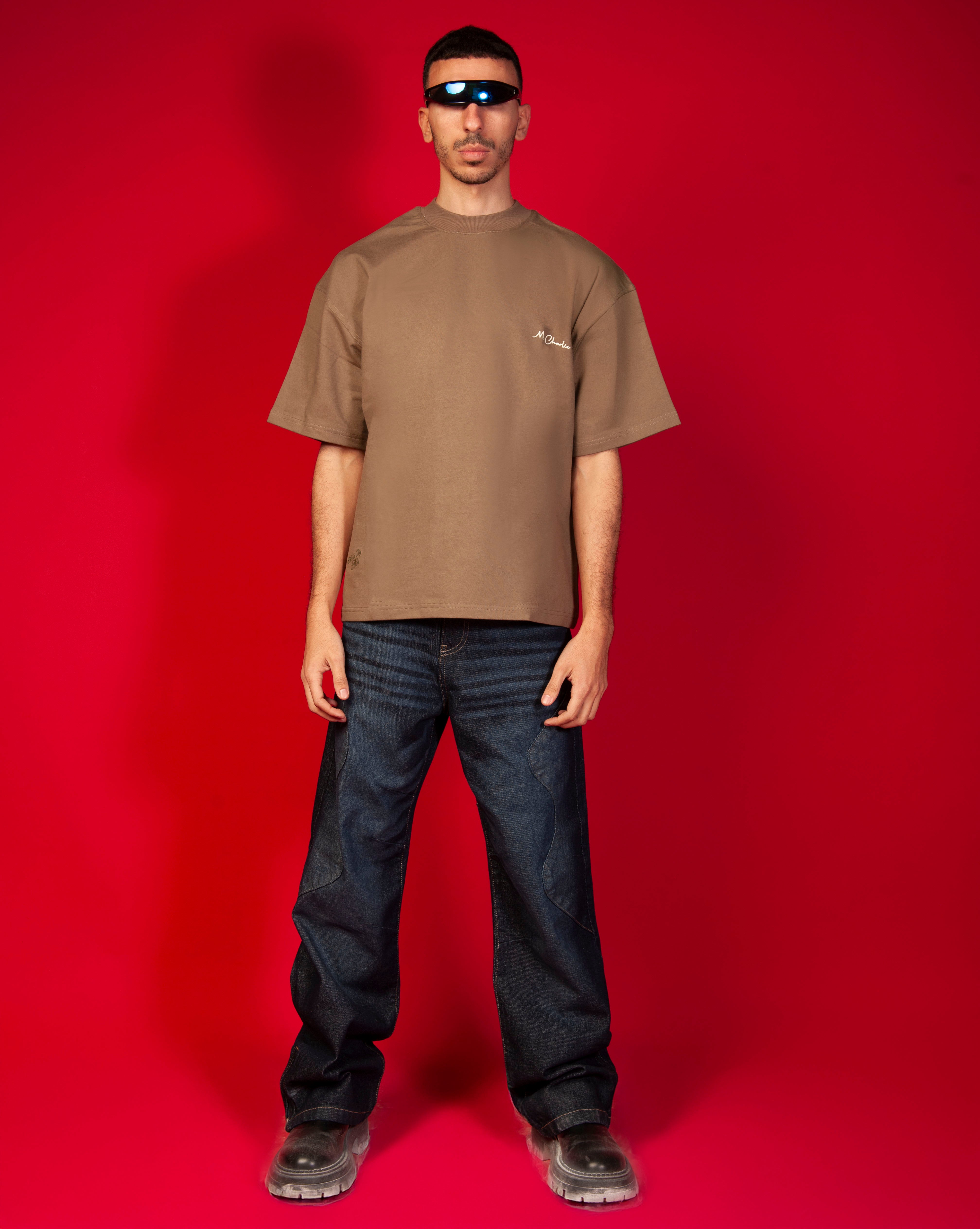 Street Rules T-Shirt MOE CHARLIE Frontansicht Ganzkoerper, camelbraunes Tee, Moe-Charlie-Brust, dunkle Jeans und Boots