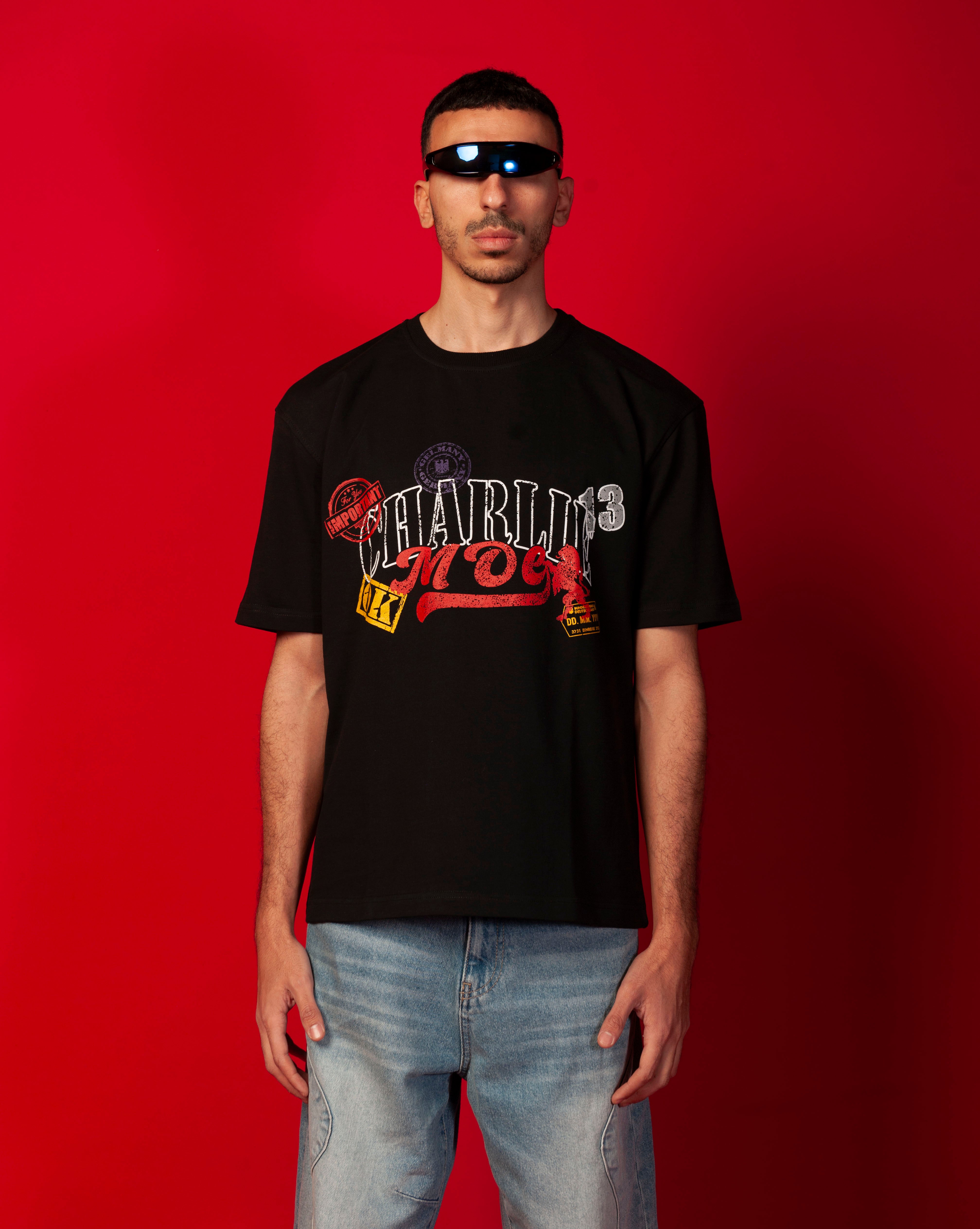 MOE CHARLIE Stampel T-Shirt Brustansicht, schwarzes Tee mit buntem CHARLIE-MOE Stempel-Print, blauer Visor-Brille