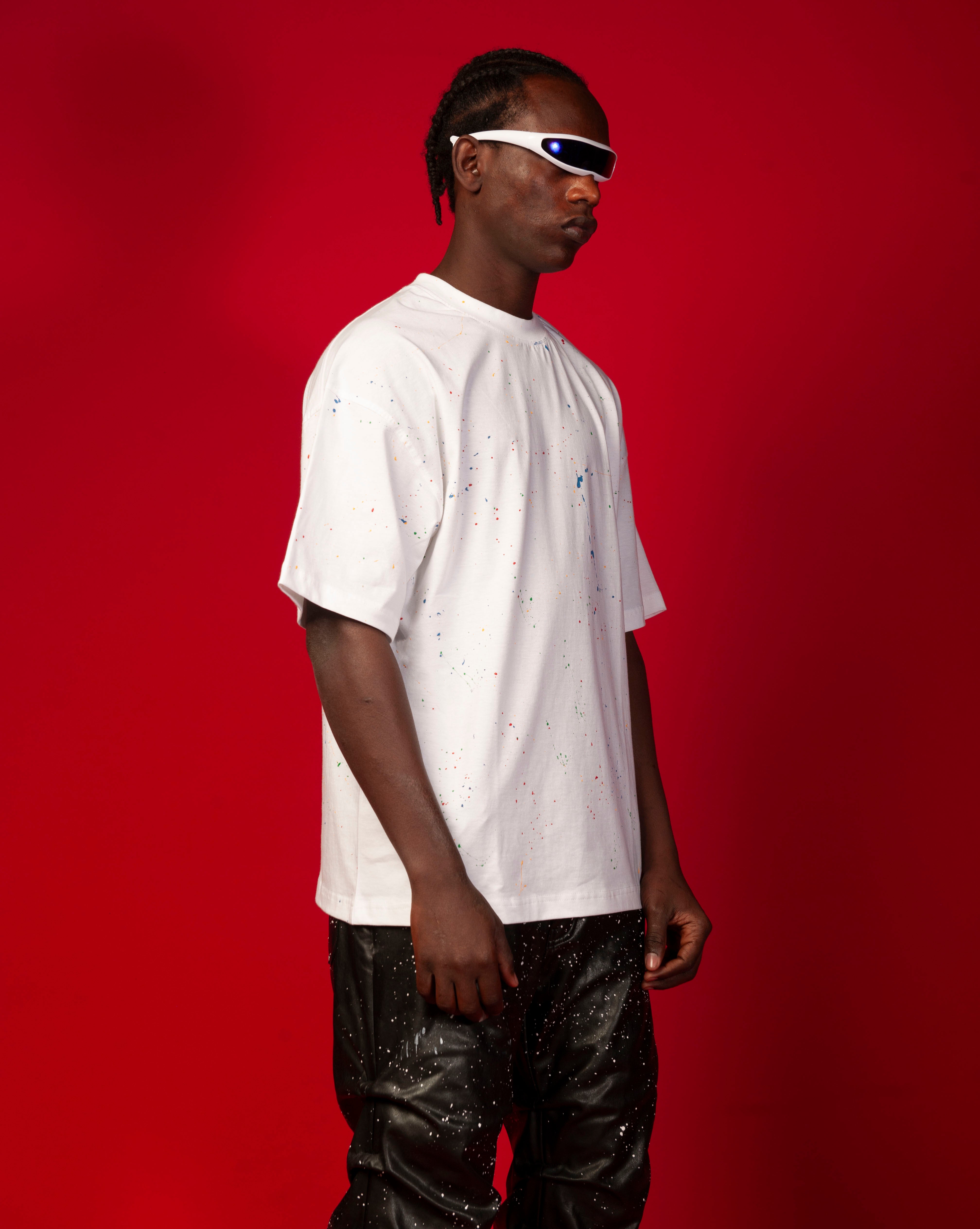 Artist T-Shirt Weiss MOE CHARLIE, Seitenansicht maennlich mit Cornrows, bunter Farbspritzer-Print und schwarze Lederhose