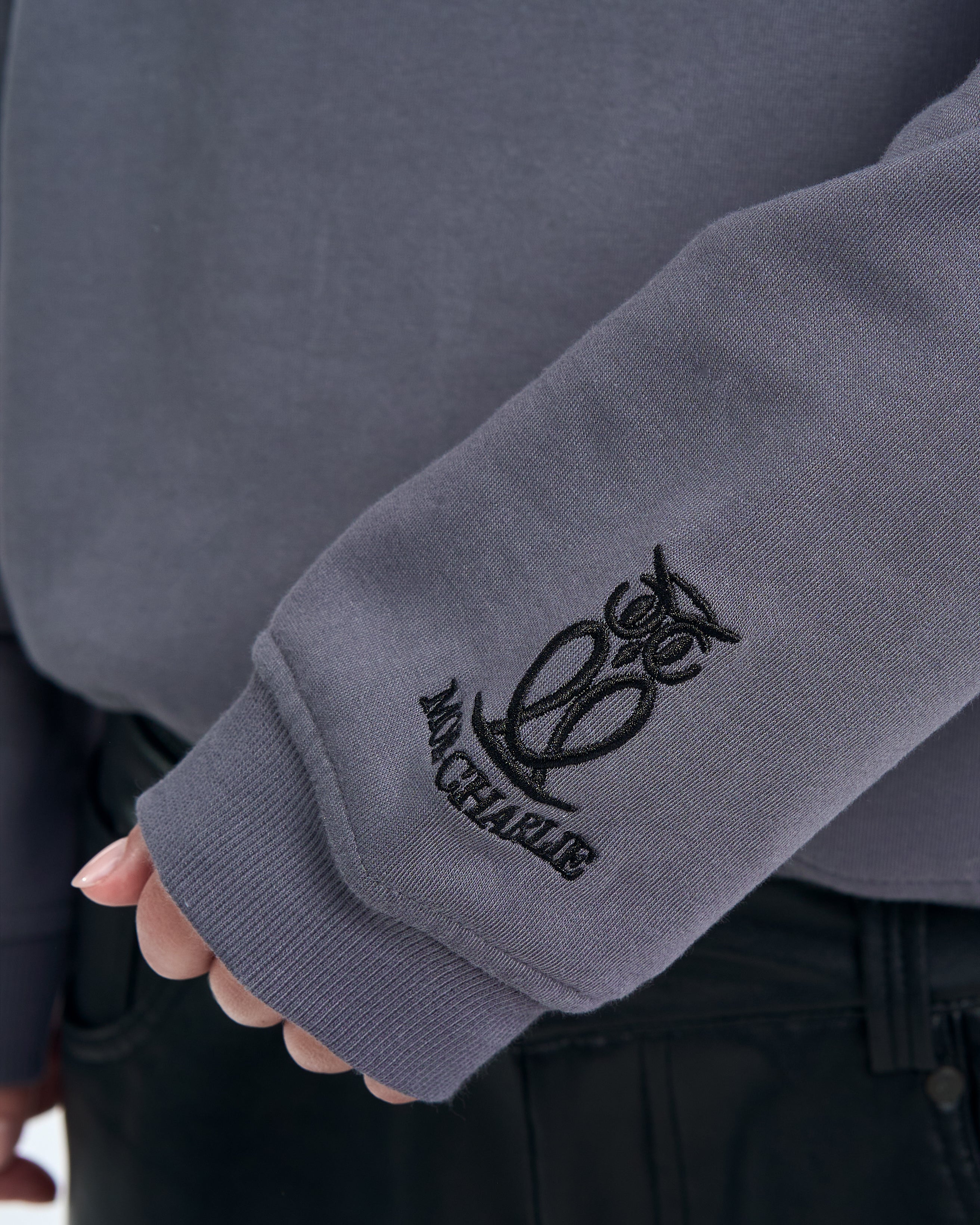 Ärmeldetail MOE CHARLIE Born in Exile Sweatshirt Grau – gesticktes Marken-Crest am Bündchen in Nahaufnahme