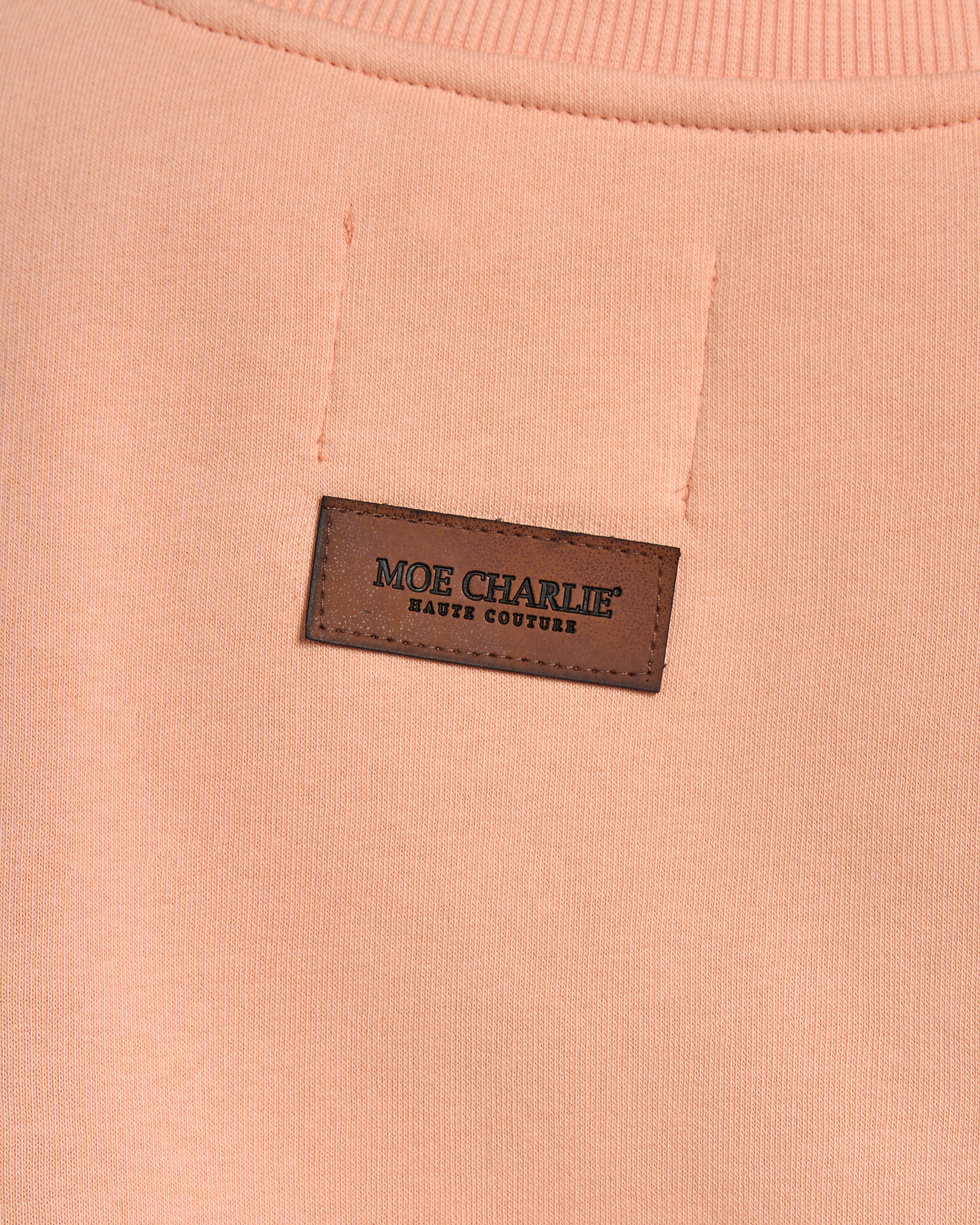 Nahaufnahme Rücken-Lederpatch – MOE CHARLIE Haute Couture Etikett auf pfirsichfarbenem Oversize-Sweater