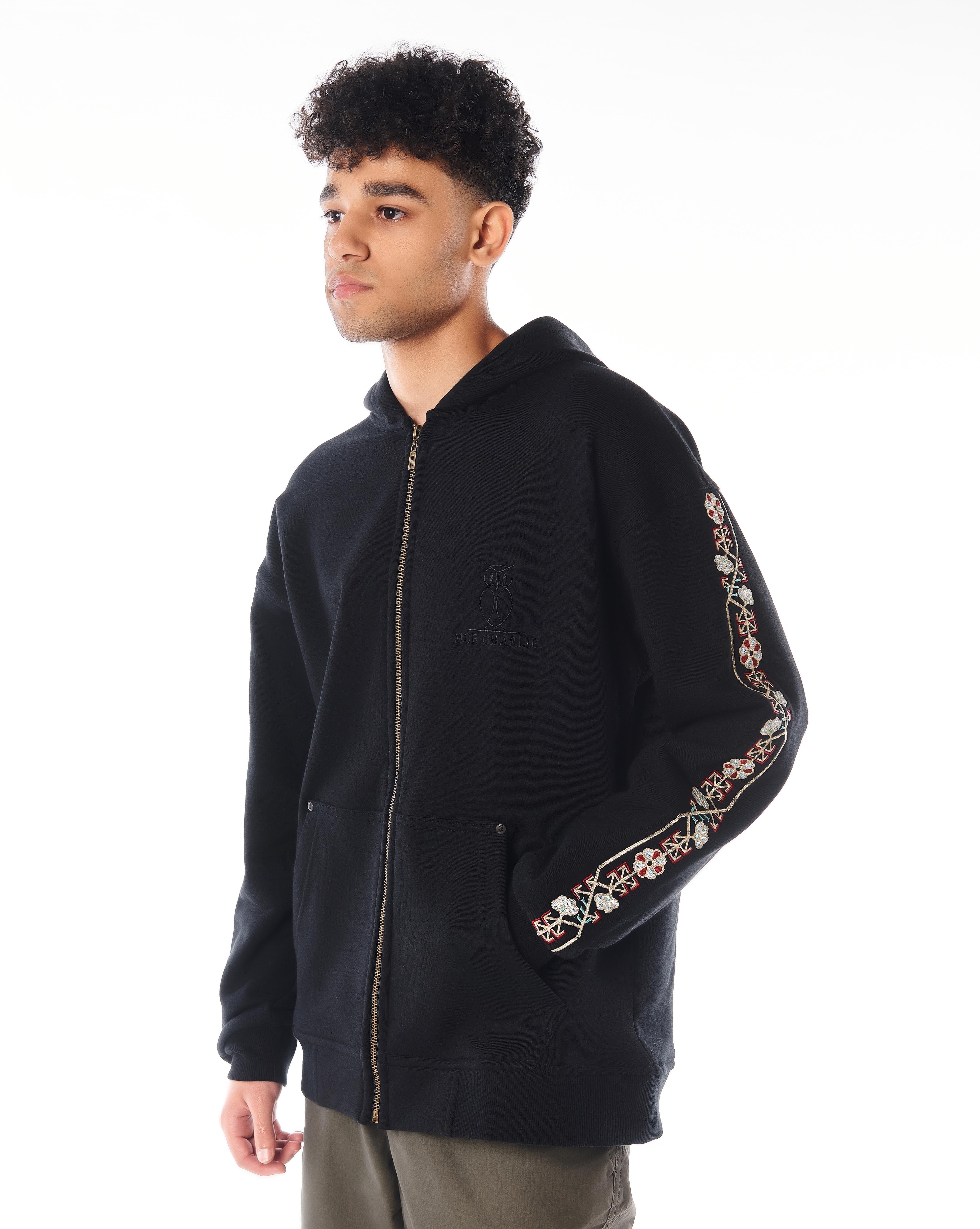 MOE CHARLIE Culture Zip-Hoodie, leicht angewinkelte Pose, Olive-Cargohose und Sneaker, Ärmelstickerei sichtbar