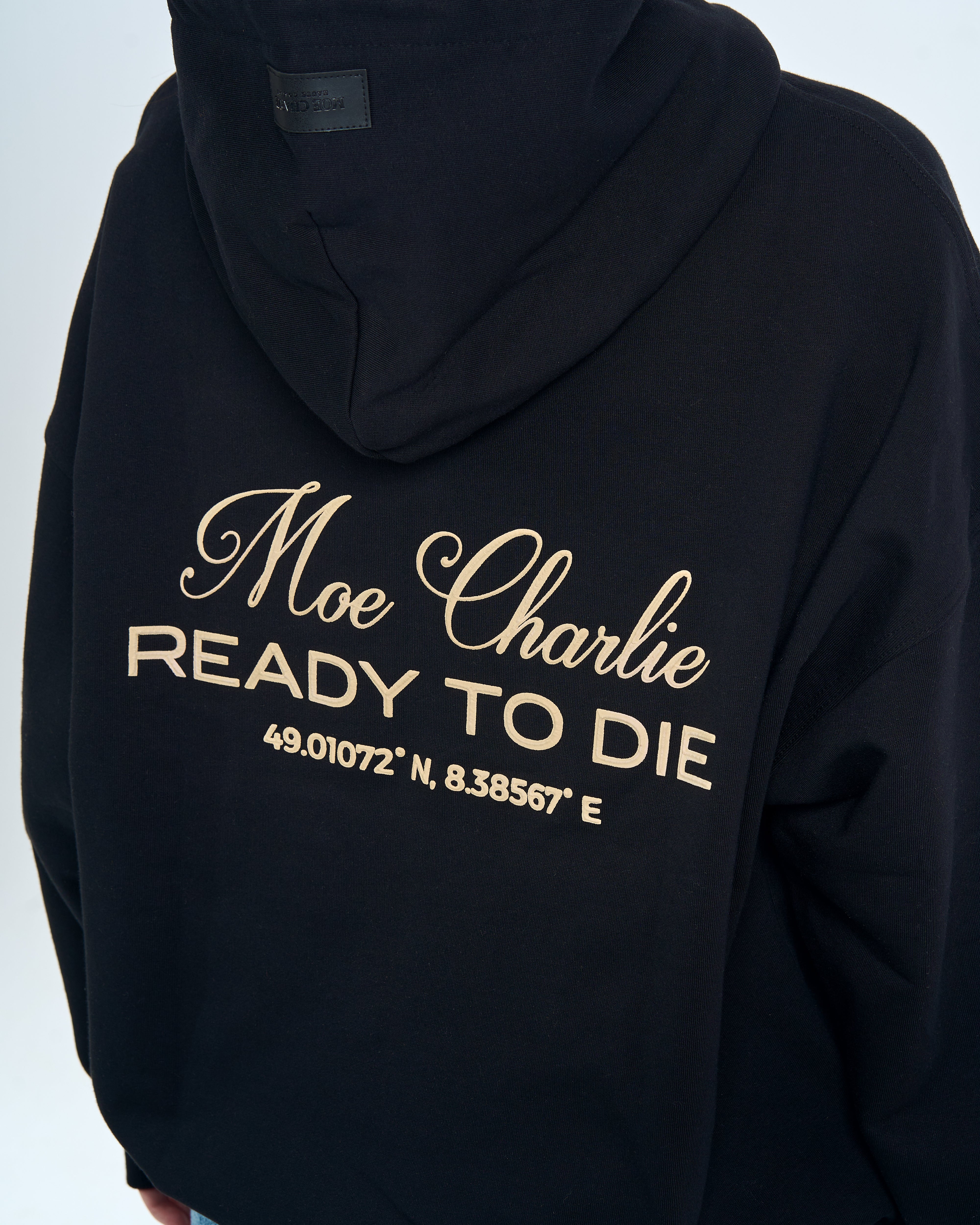 Nahaufnahme Rückendruck Ready to Die, MOE CHARLIE – Goldschrift mit Koordinaten auf schwarzem Hoodie