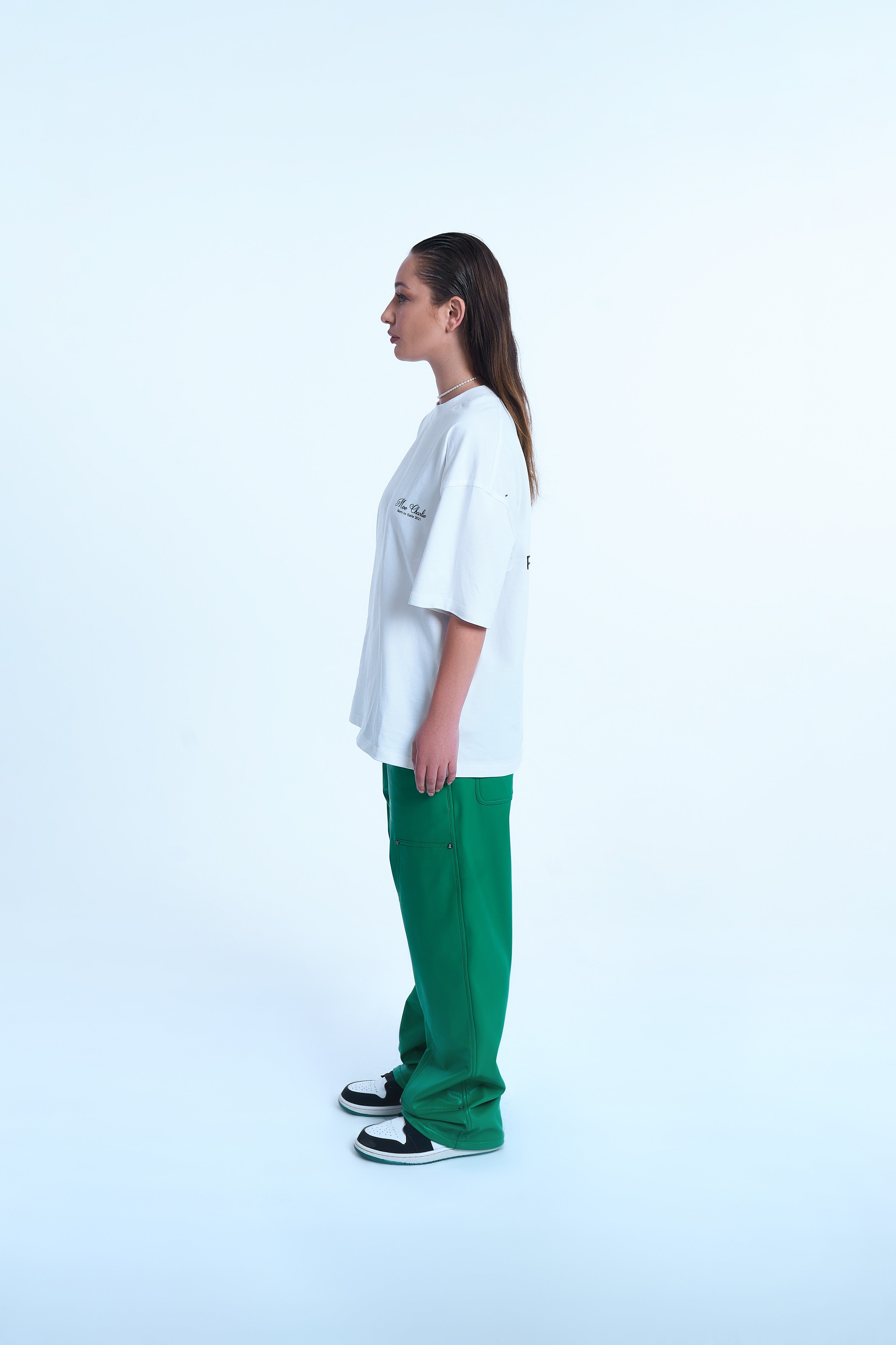 Seitenansicht weiblicher Model MOE CHARLIE Ready To Die Weiß – Rückenprint seitlich erkennbar, grüne Lederhose