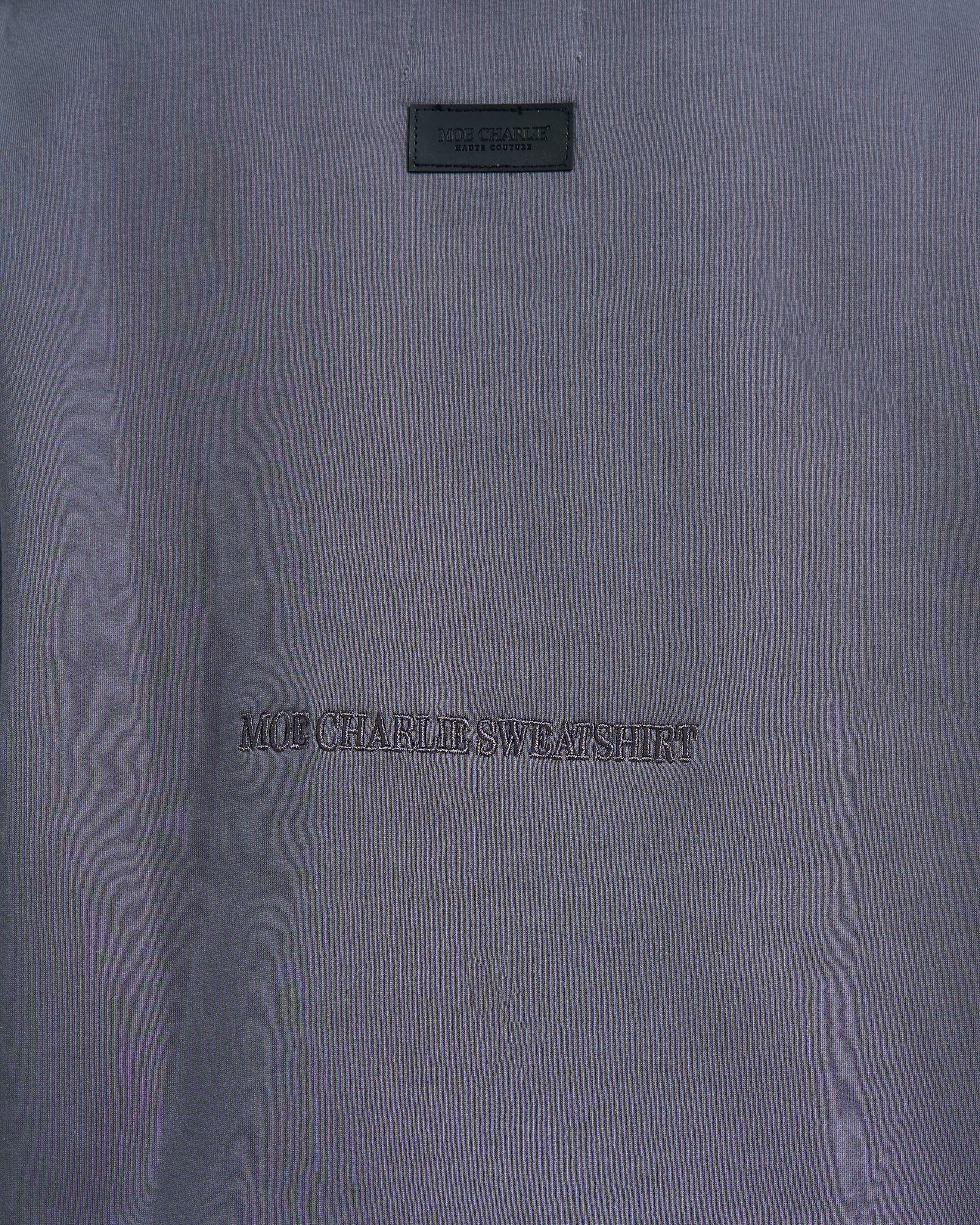 Nahaufnahme MOE CHARLIE SWEATSHIRT Stickerei auf grauem Stoff – tonale Buchstabenprägung in Detailansicht