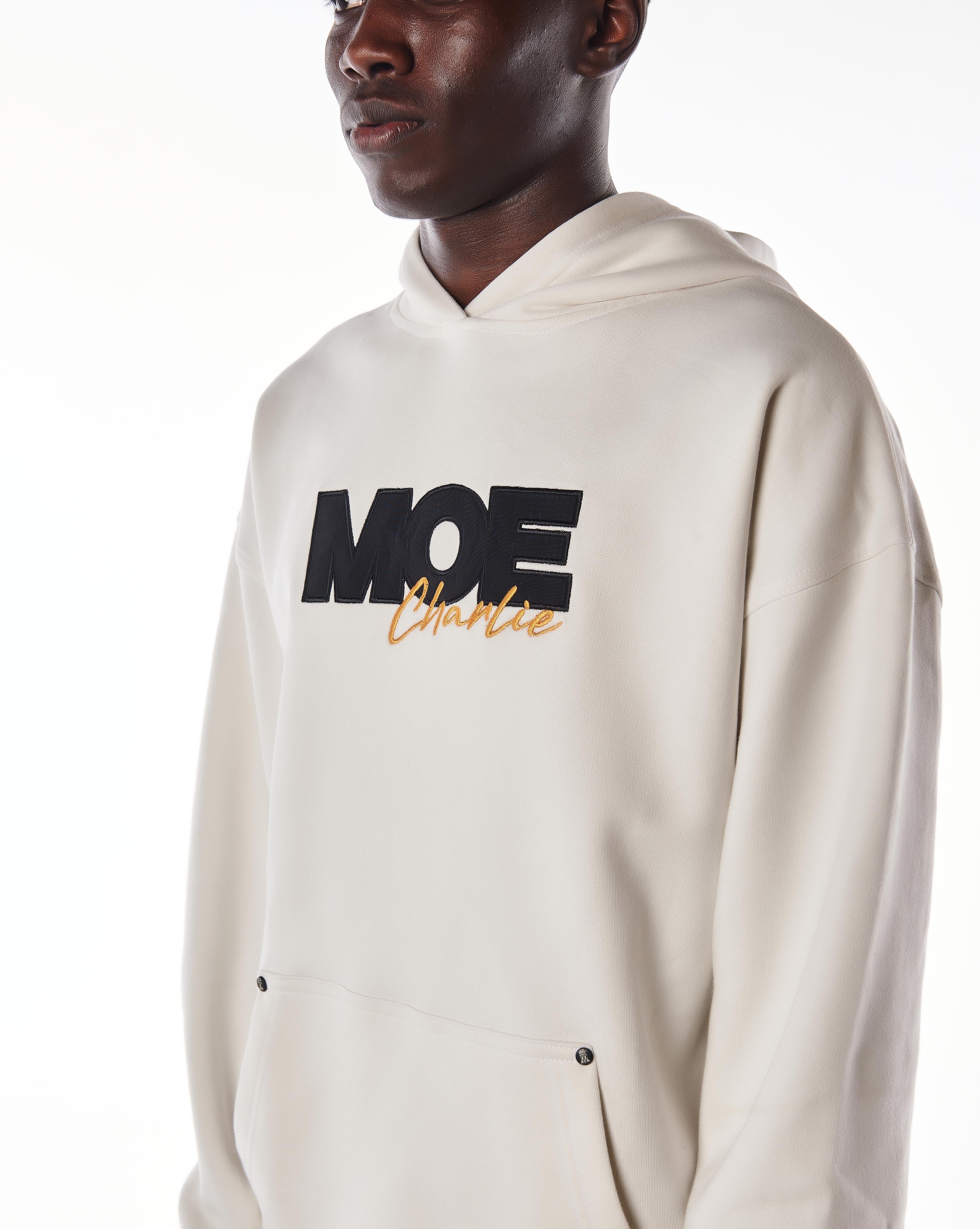 Nahaufnahme Brust-Stickerei MOE CHARLIE Gold Passion Hoodie, schwarze MOE-Buchstaben, goldener Charlie-Schrift