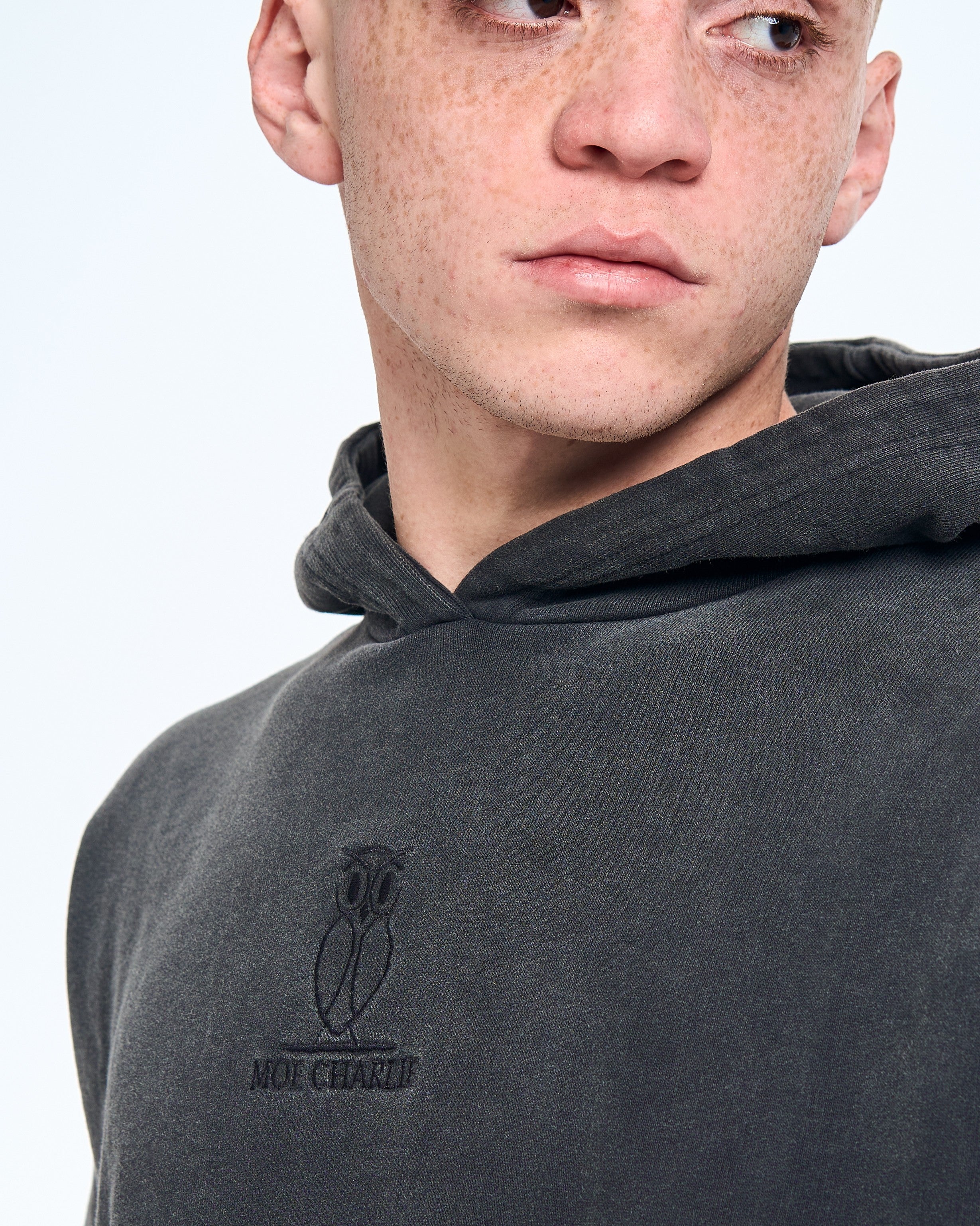 Detailaufnahme Owl-Crest-Stickerei MOE CHARLIE auf vintage-verwaschenem Hoodie-Stoff in Fade-Out-Schwarz