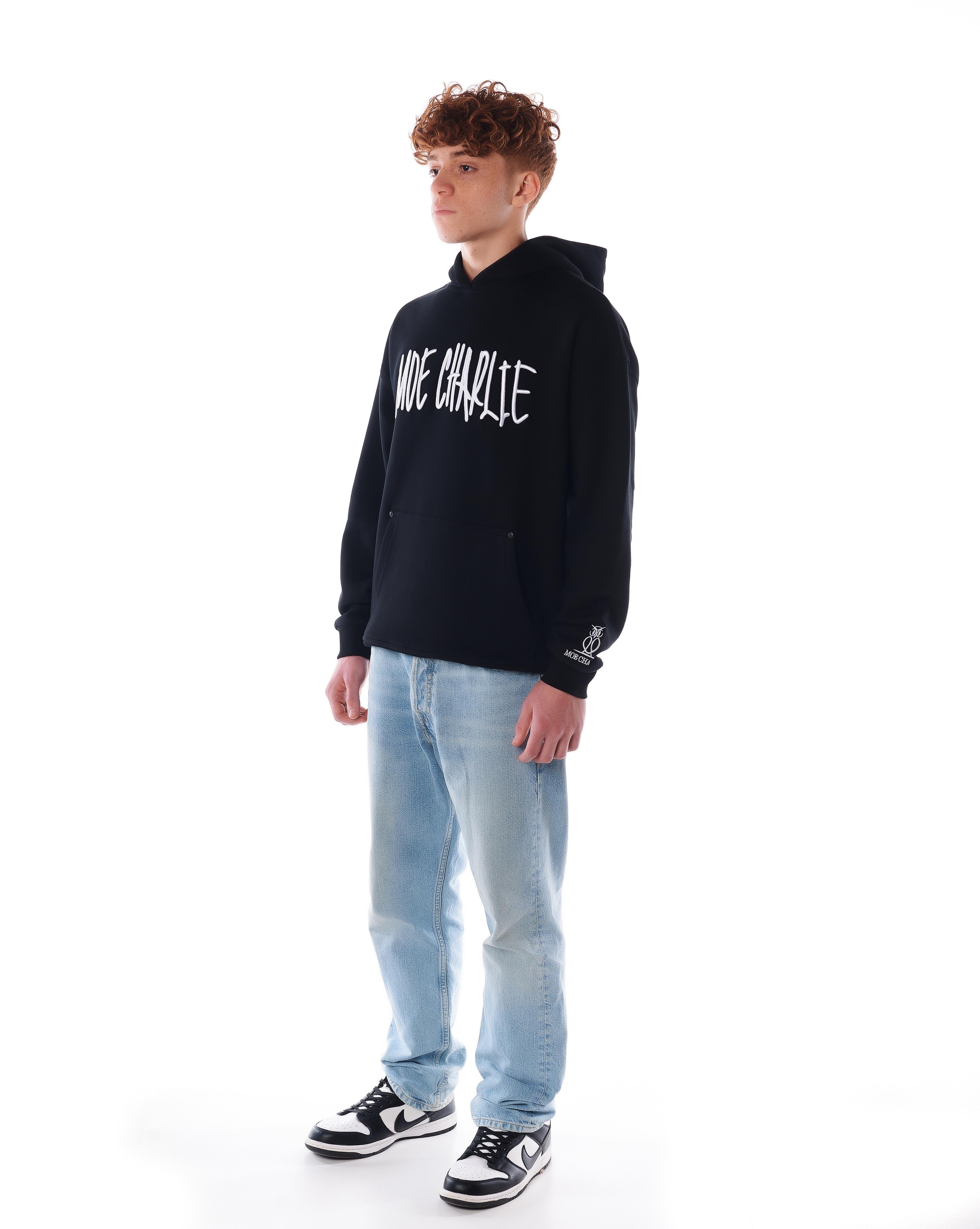 MOE CHARLIE Night Life Hoodie, leichte Frontansicht von links, Graffiti-Schriftzug auf der Brust, Jeans und Nike-Sneaker