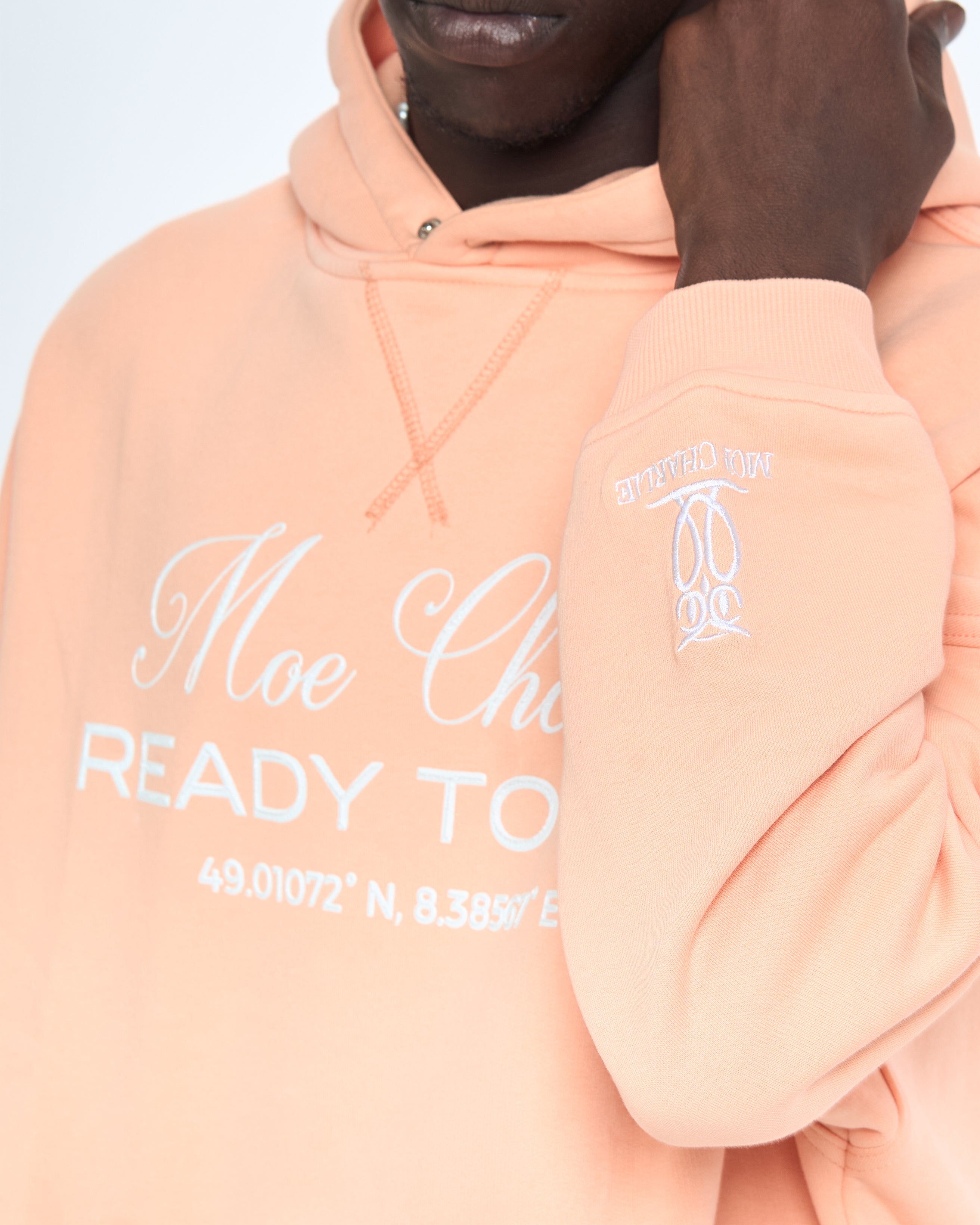 Nahaufnahme Ready to Die Hoodie MOE CHARLIE Peach – Frontprint und Sleeve-Logo, Hand an der Kapuze