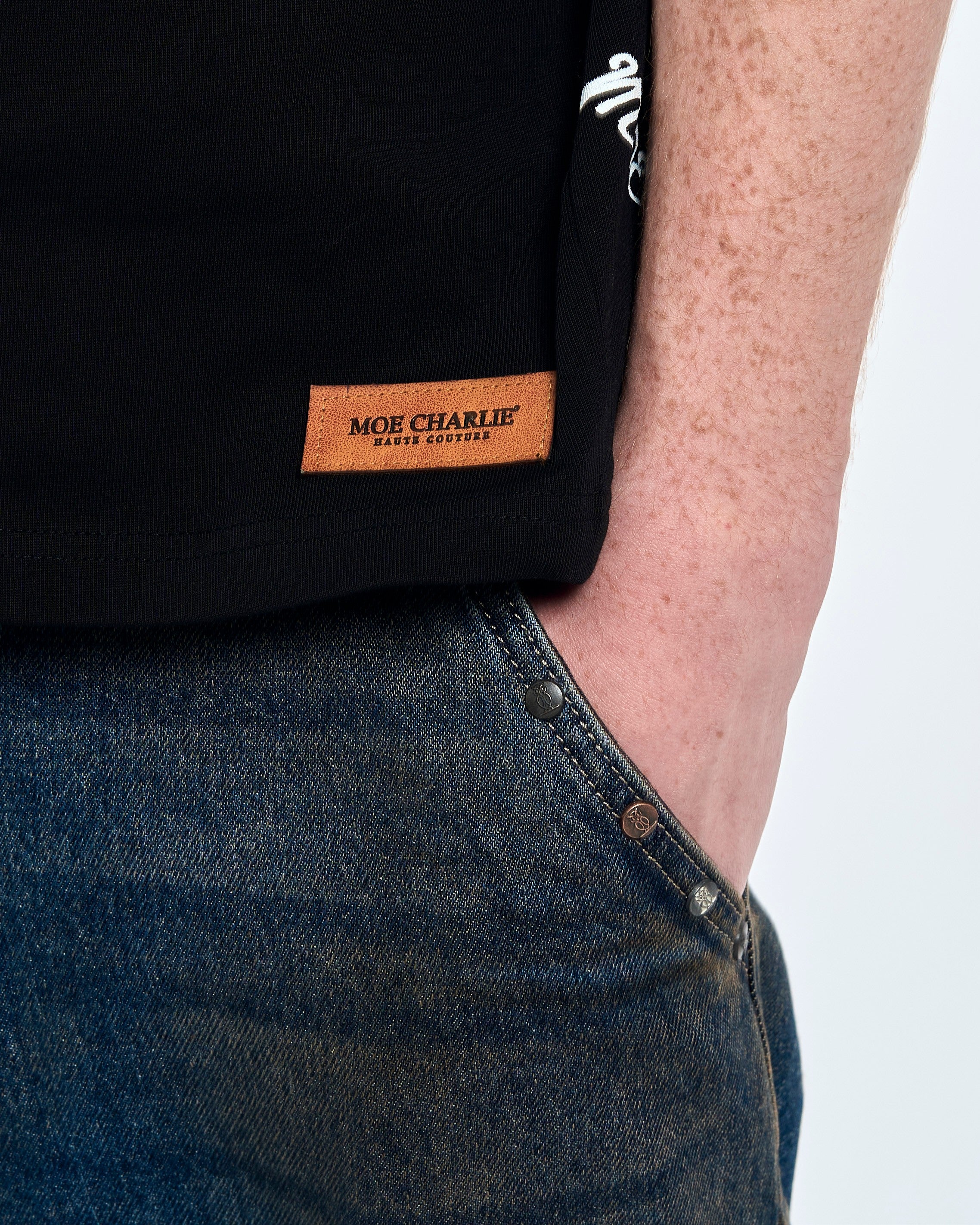 Zweite Nahaufnahme Lederpatch - MOE CHARLIE Haute Couture Etikett am Saum des schwarzen Forbidden T-Shirts