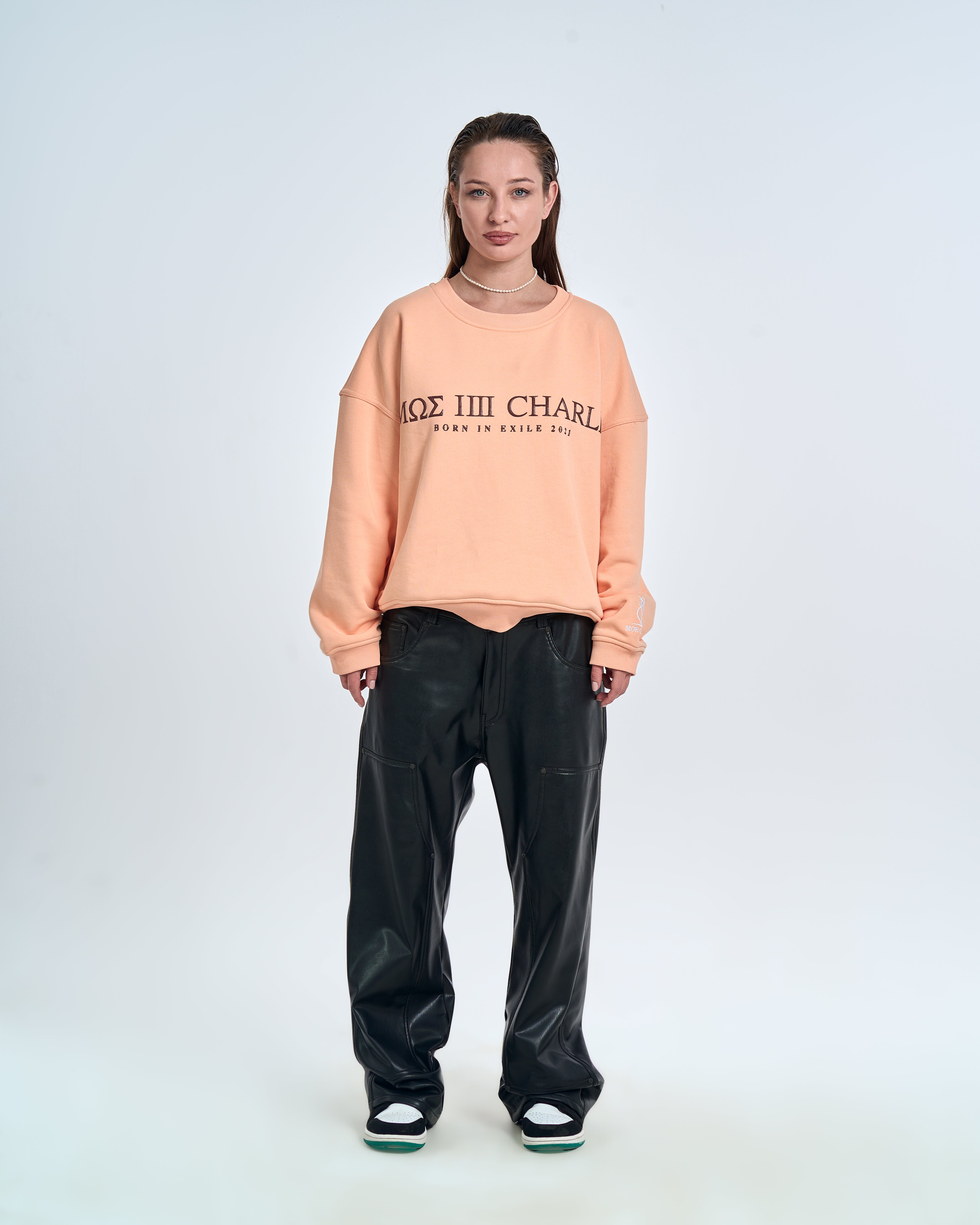 MOE CHARLIE Born In Exile Sweater Peach – Frontansicht Damenmodel, MΩΣ-Print, schwarze Lederhose, Jordan Sneaker