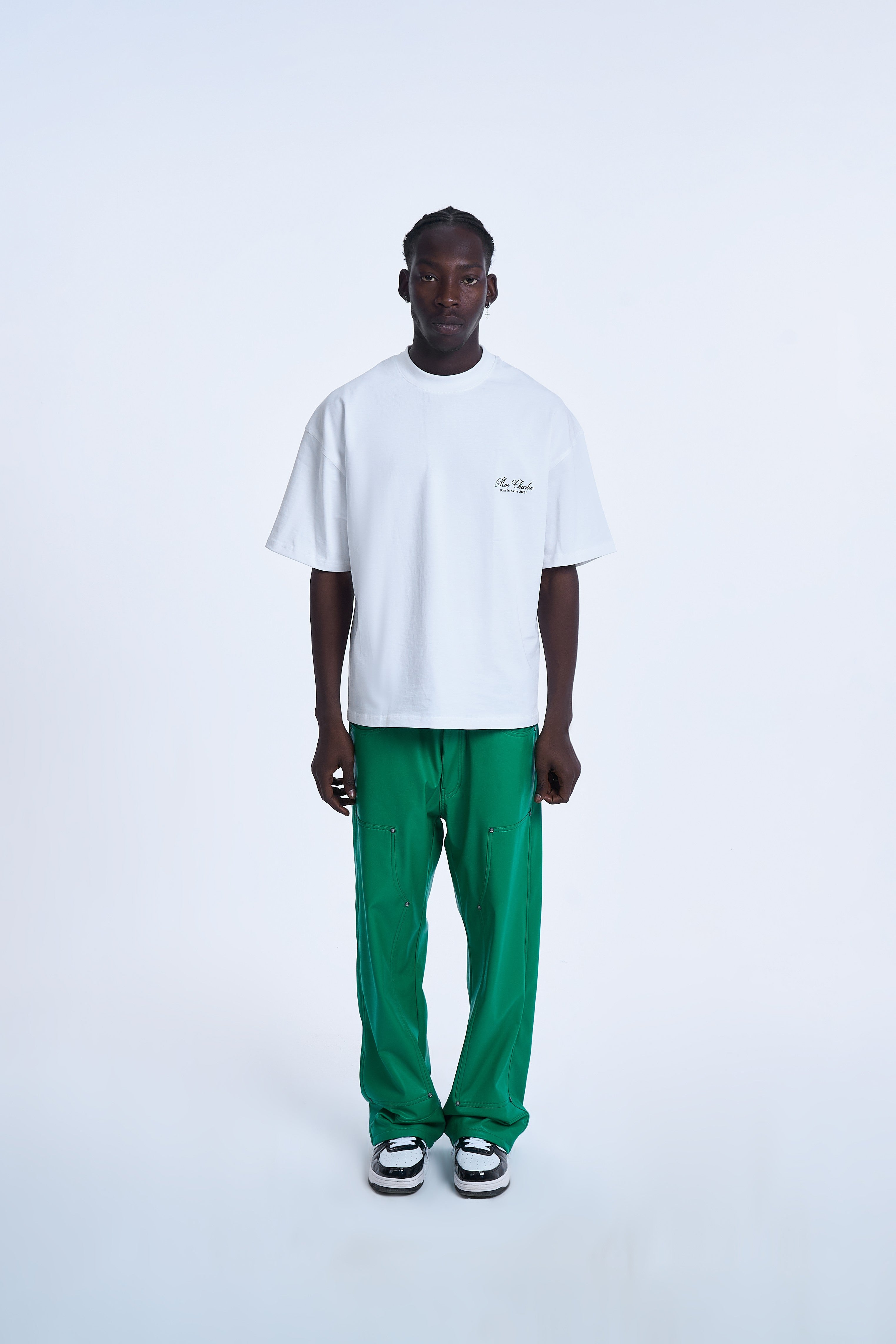 Mann trägt MOE CHARLIE Ready To Die T-Shirt in Weiß mit Script-Brustlogo, kombiniert mit grünen Leather-Pants