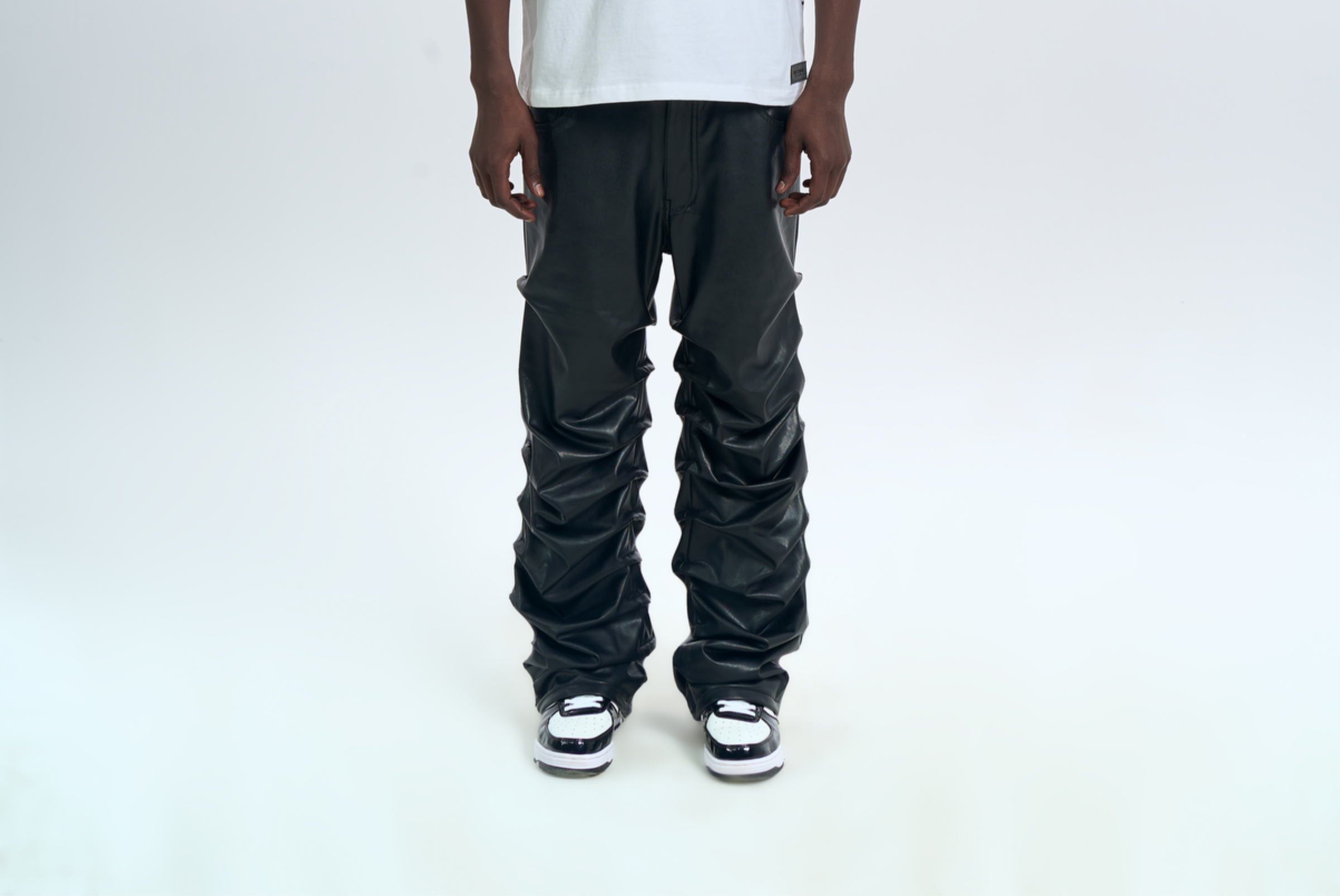 MOE CHARLIE Crow Leather Pants Schwarz, Frontansicht ab Hueft, dramatische Faltenstruktur am Bein, Sneakers