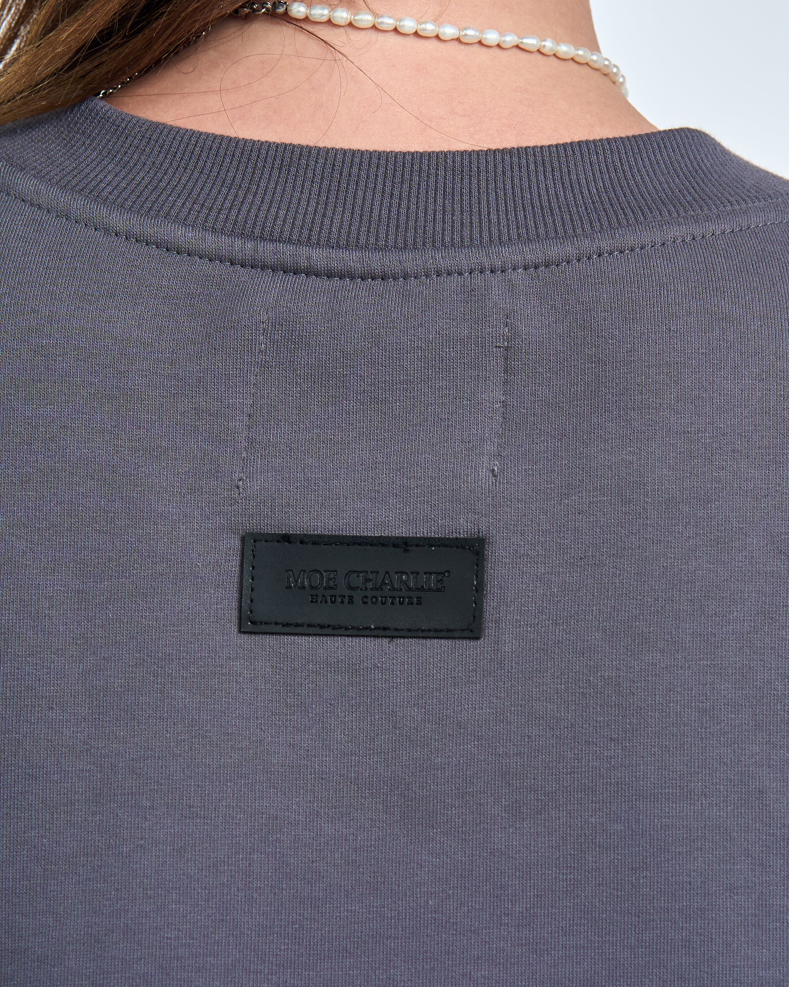 Detailaufnahme Leder-Etikette MOE CHARLIE HAUTE COUTURE auf dem Rückenausschnitt des grauen Sweatshirts