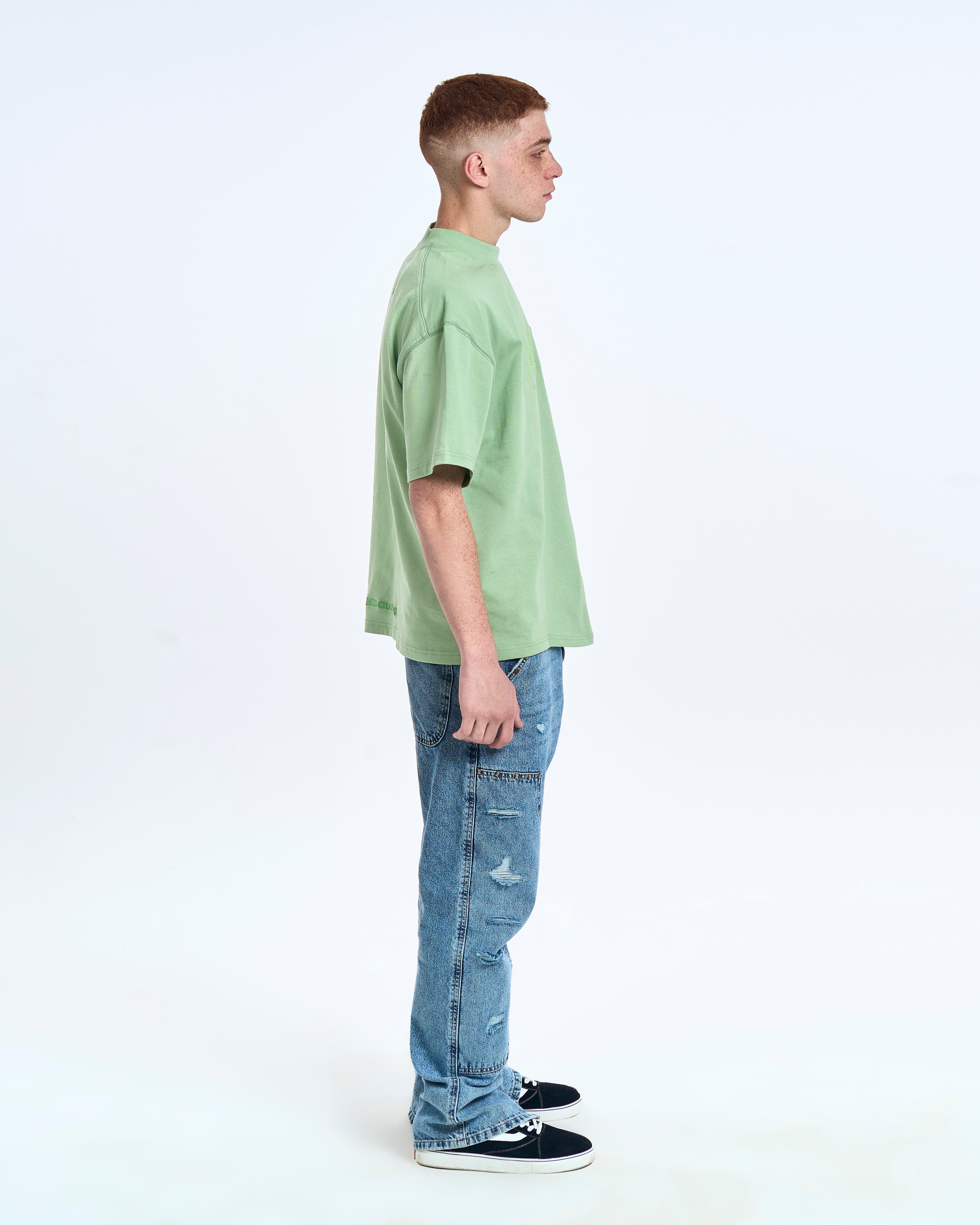 MOE CHARLIE Born In Exile T-Shirt Mintgrün – Seitenansicht links, Saum-Stickerei sichtbar, blaue Carpenter-Jeans