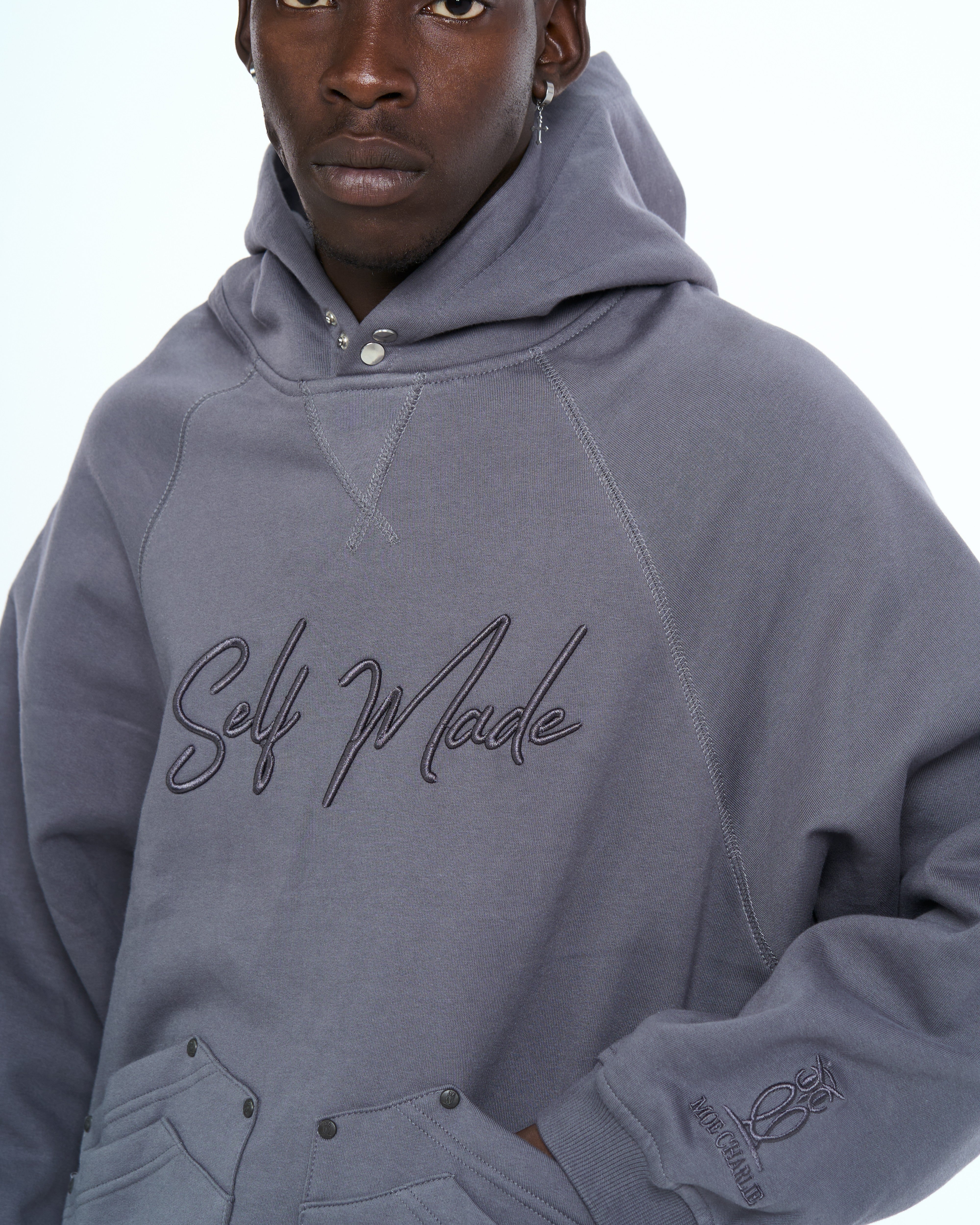 Nahaufnahme Cangaroo Hoodie MOE CHARLIE in Grau, Brustbereich mit Self-Made-Schriftzug und Sleeve-Logo