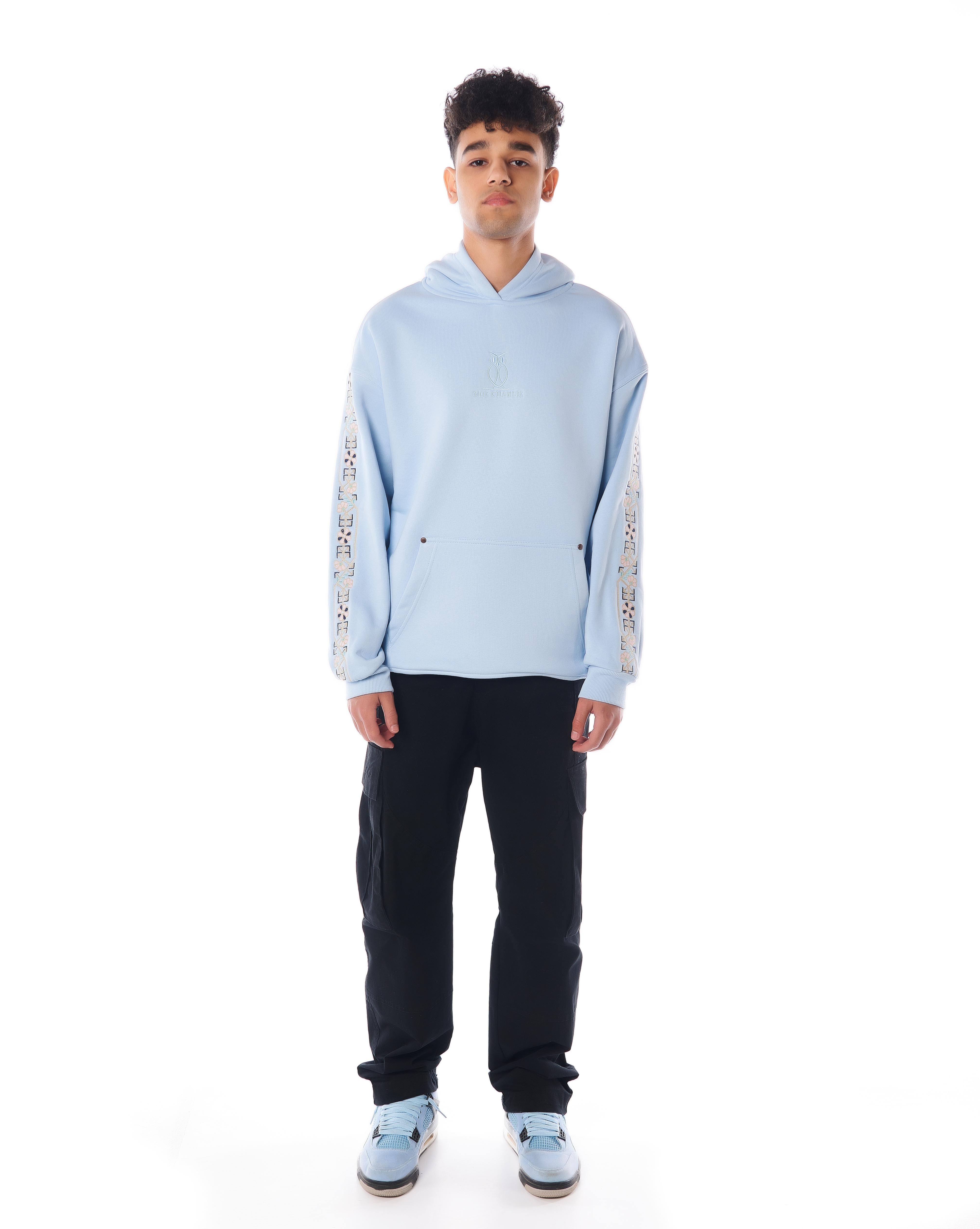 MOE CHARLIE The Culture Hoodie Riviera Blue, Frontpose mit floraler Ärmel-Stickerei und schwarzer Cargohose