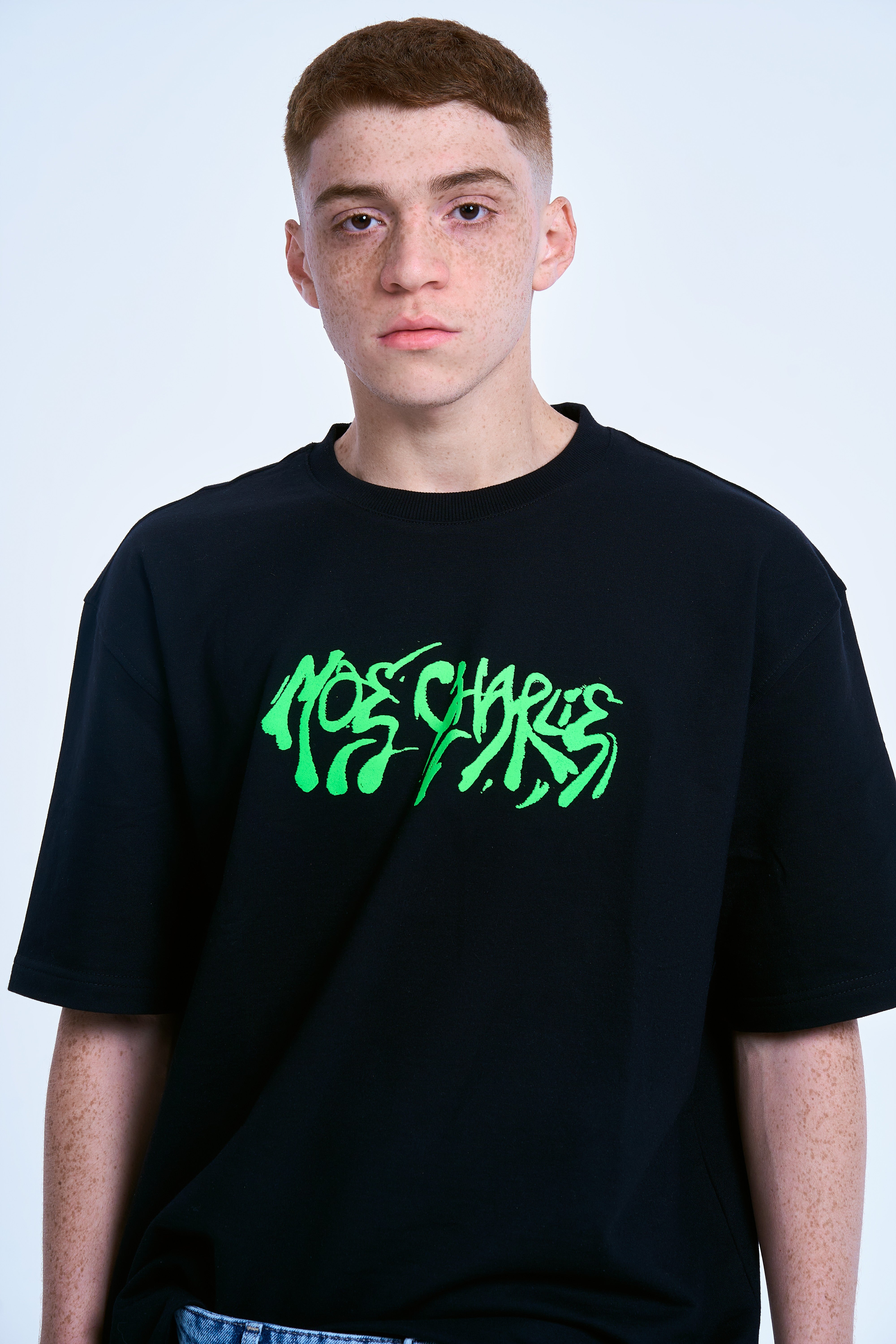 Nahaufnahme MOE CHARLIE Graffiti T-Shirt, grüner Schriftzug-Print im Fokus, direkter Blick, Frontansicht