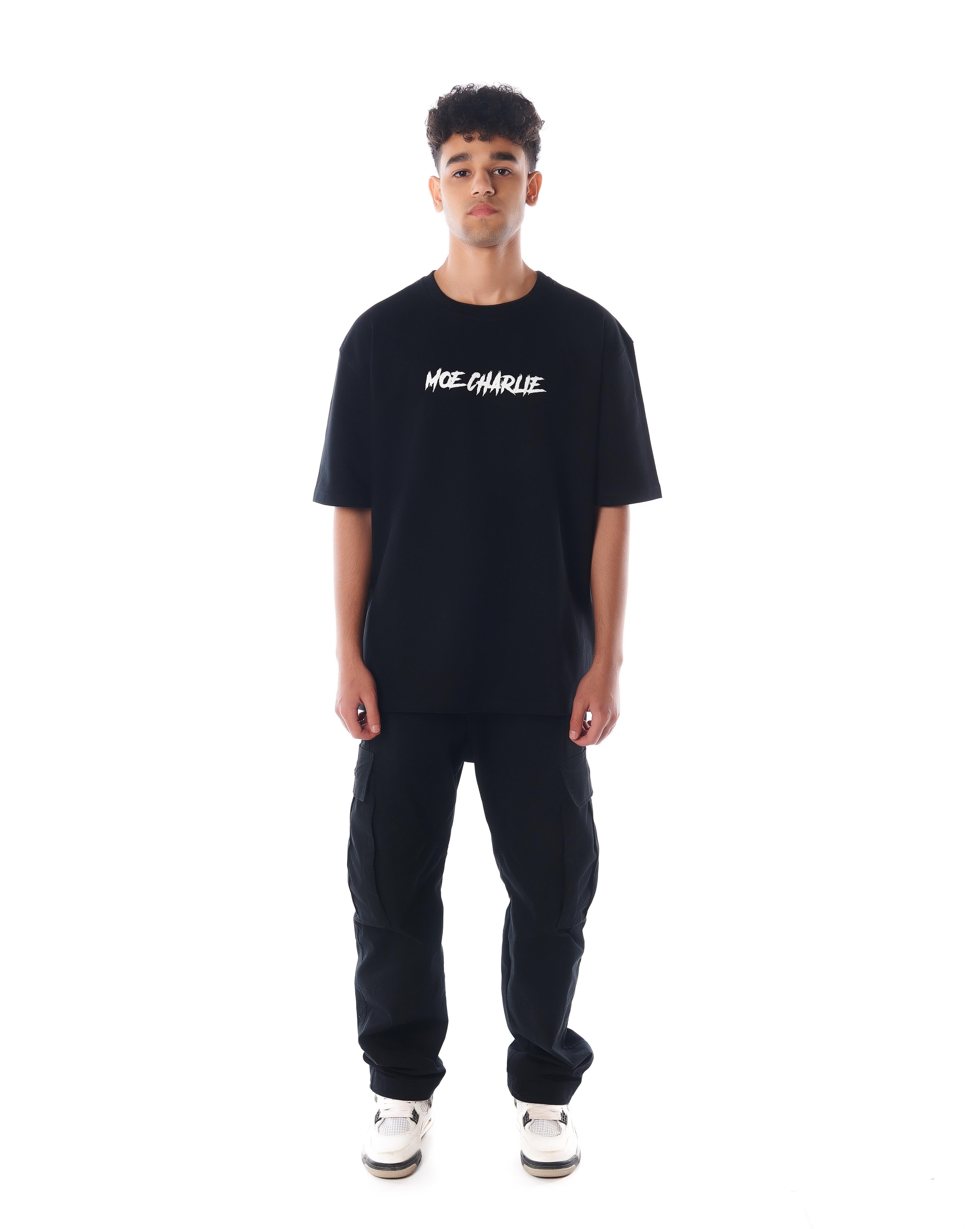 Frontansicht MOE CHARLIE Predator T-Shirt in Schwarz, weißer Puff-Schriftzug auf der Brust, schwarze Cargo-Hose