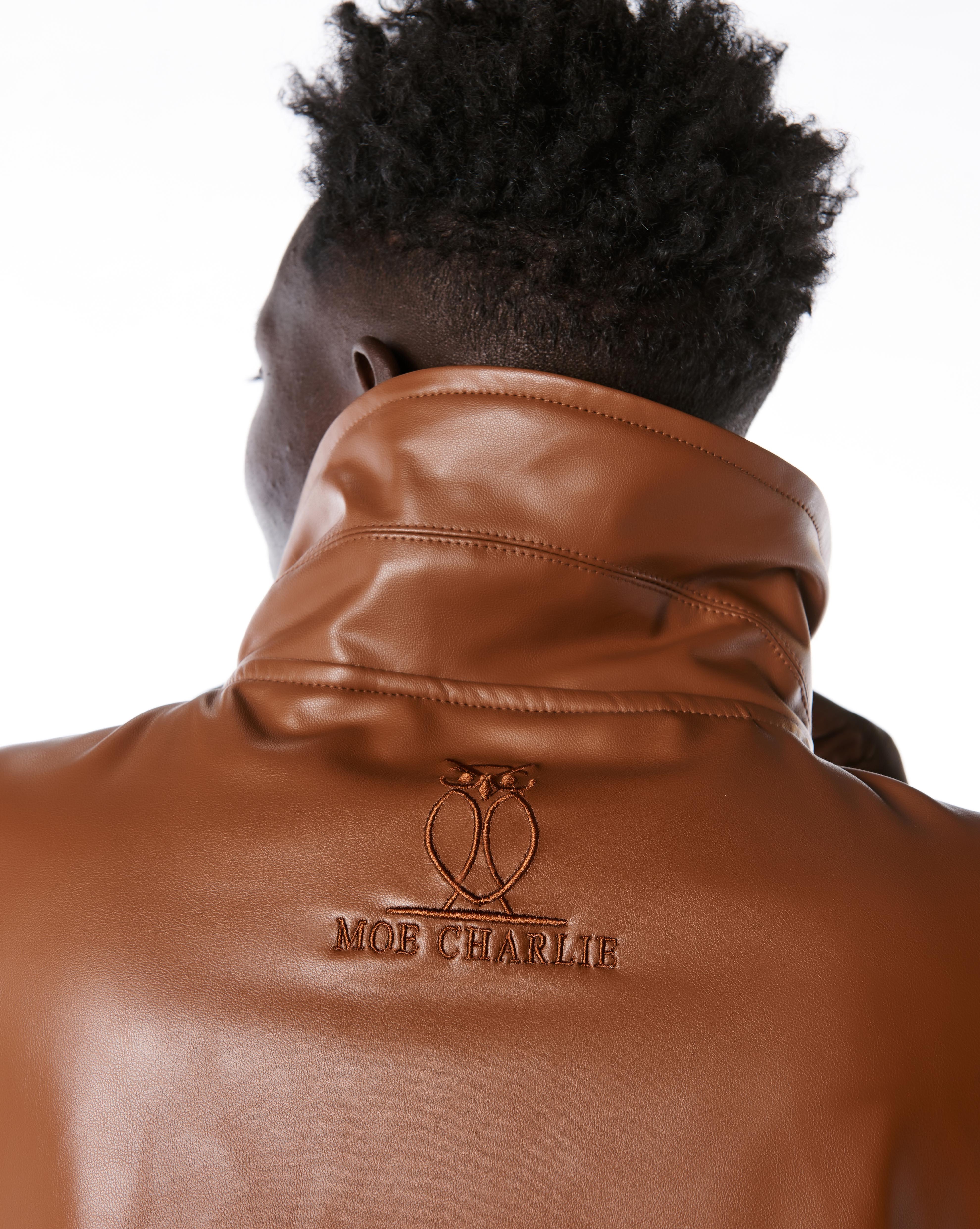 Nahaufnahme des ton-in-ton MOE CHARLIE Owl-Logos auf dem Rückenkragen der braunen Lederjacke