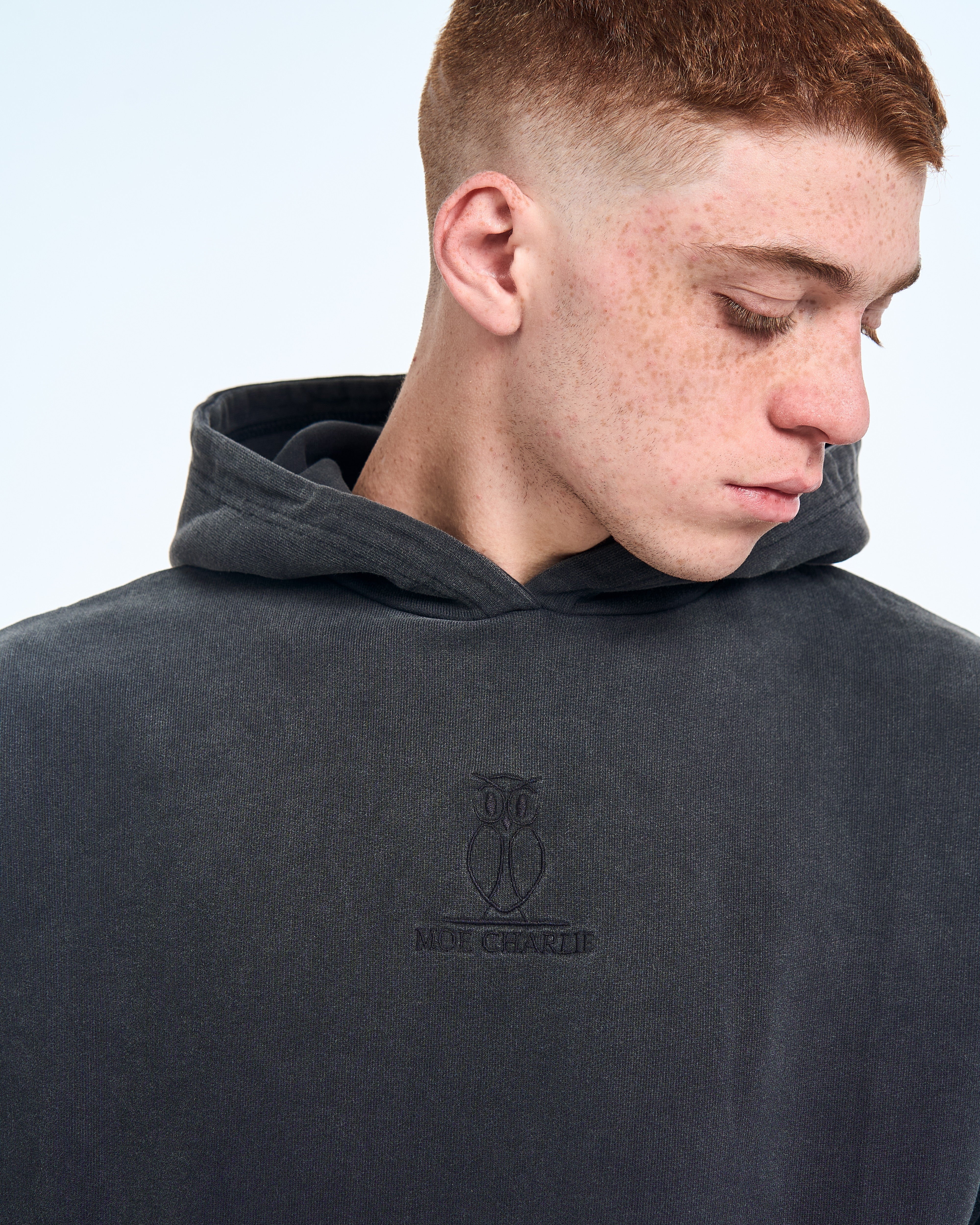 Nahaufnahme MOE CHARLIE Hoodie Fade Out Black, Brustansicht mit gesenktem Blick, Owl-Crest-Stickerei