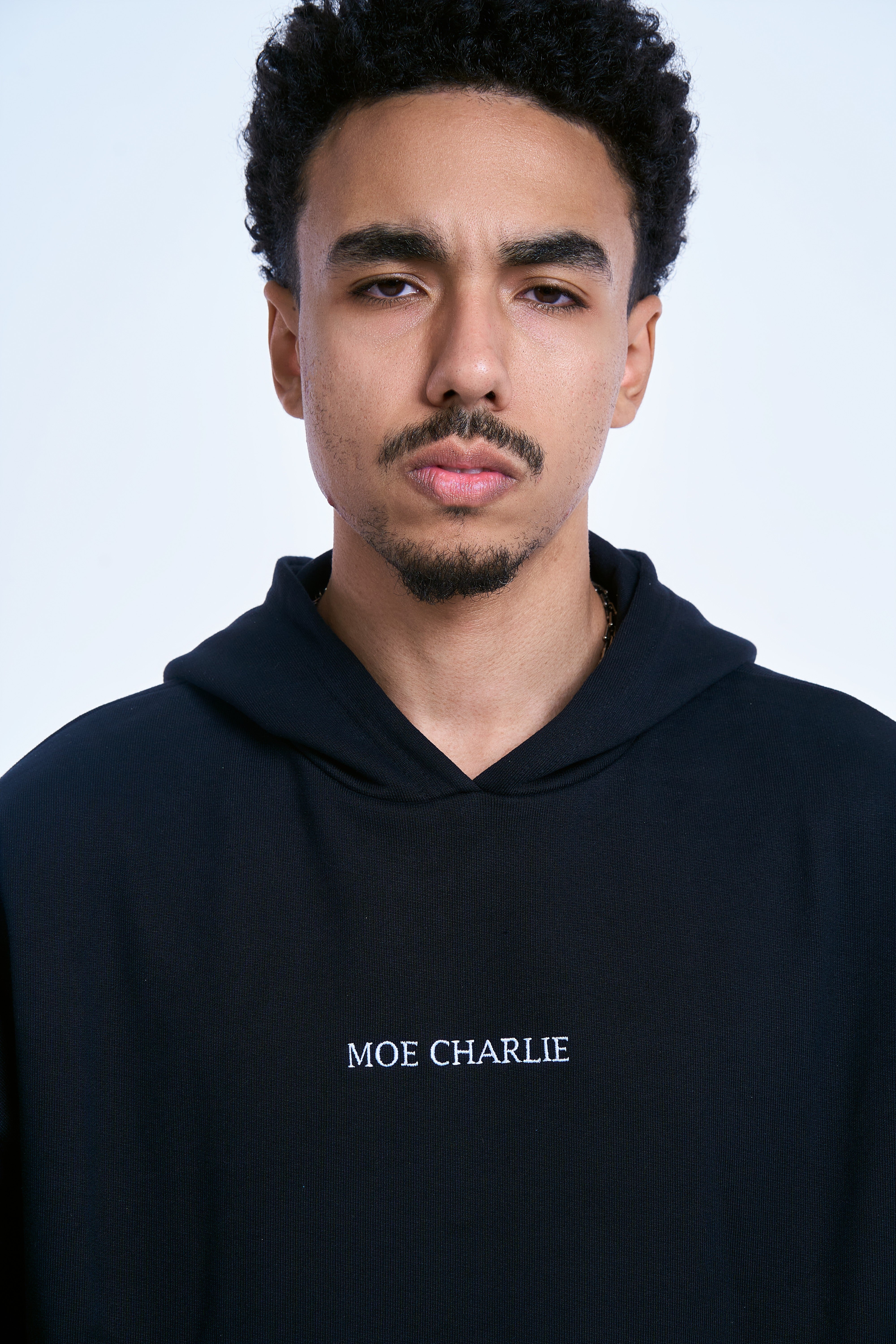 Nahaufnahme MOE CHARLIE Hoodie Schwarz - MOE CHARLIE Bruststickerei im Fokus, maennlicher Traeger mit Kette