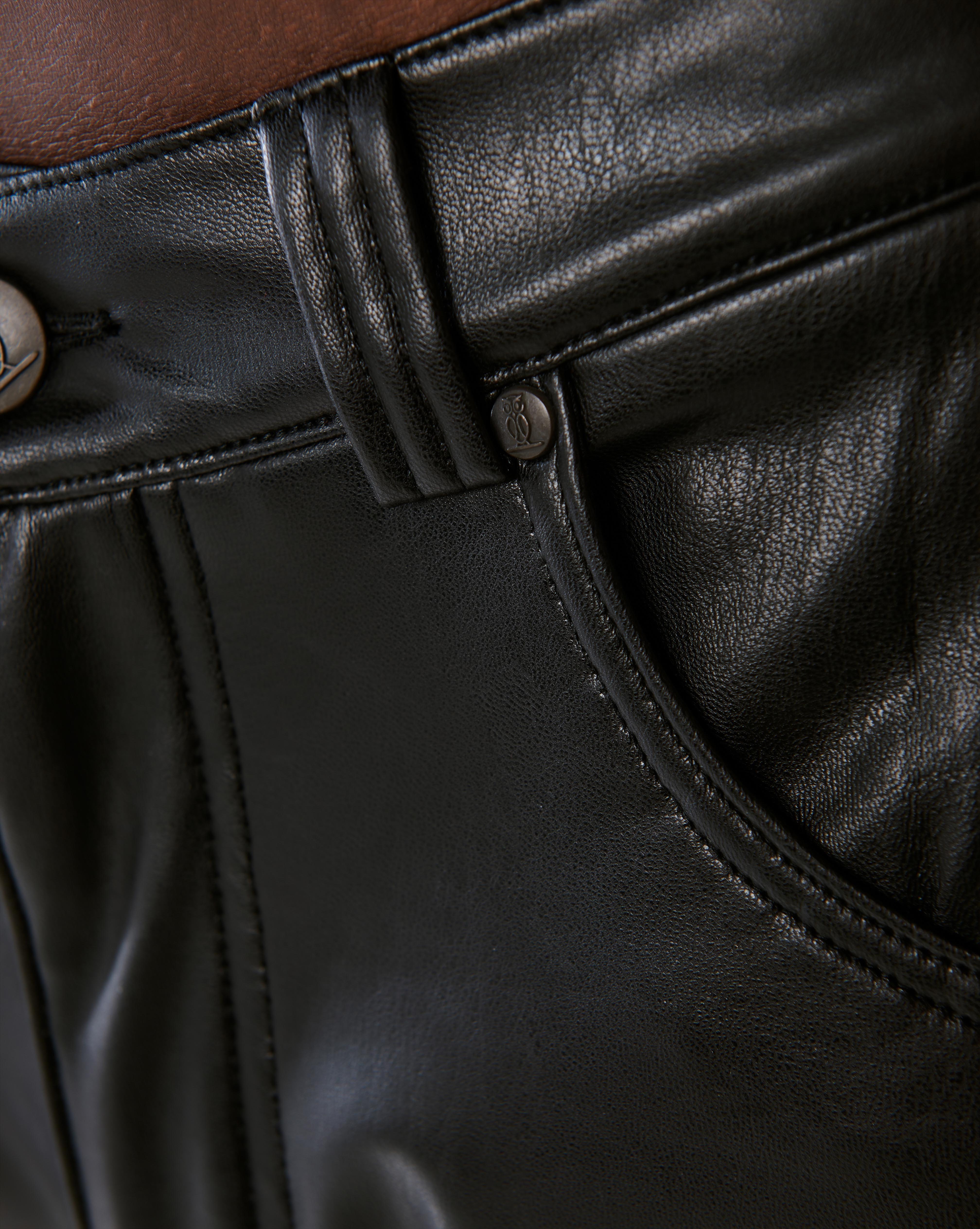 Nahaufnahme der vorderen Gürtellinie der MOE CHARLIE Lederhose Schwarz, gravierter Knopf und Taschenöffnung im Detail