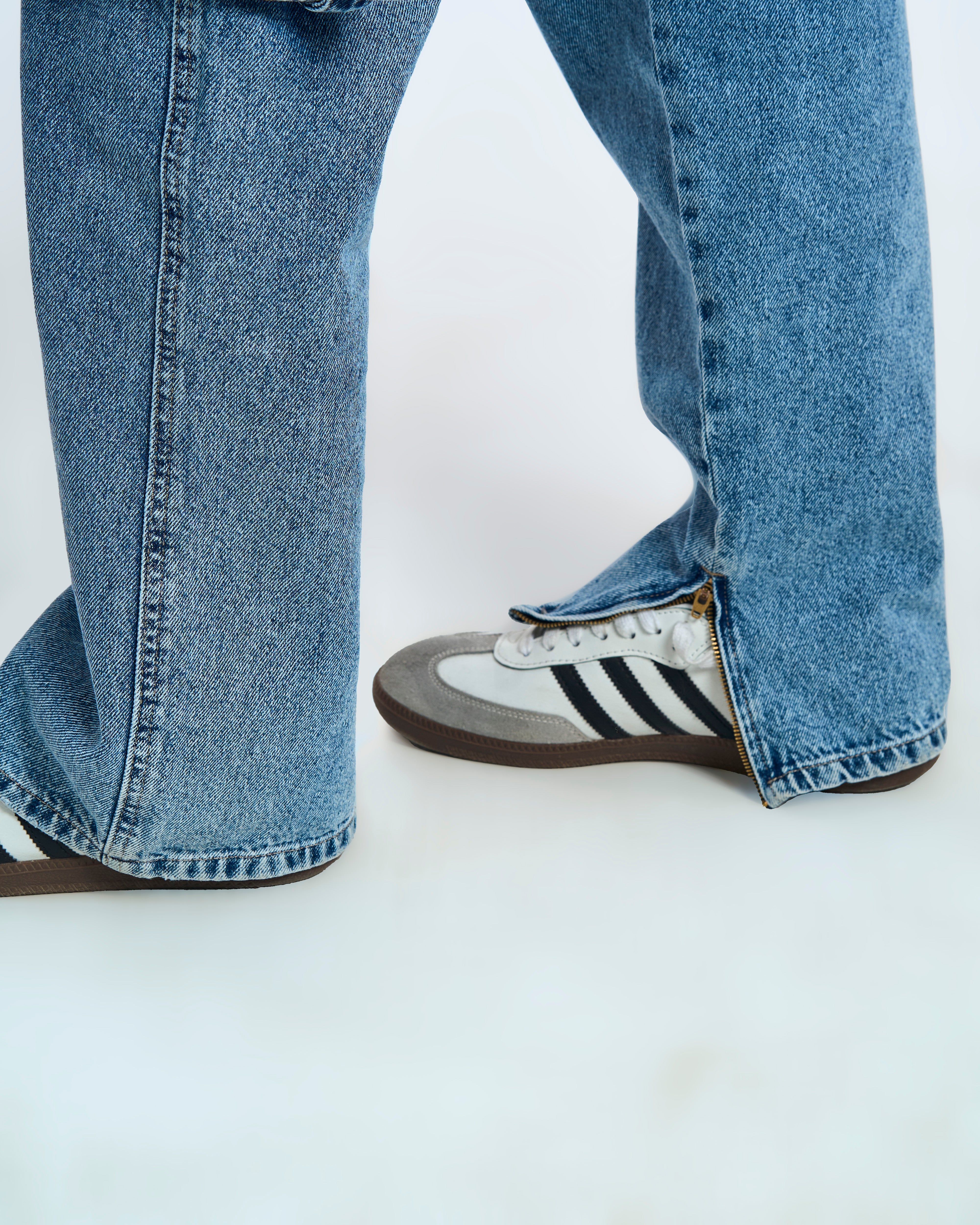 Saum-Detail der MOE CHARLIE Ice Cargo Denim – goldener Knöchel-Zipper halb offen, kombiniert mit Adidas Samba
