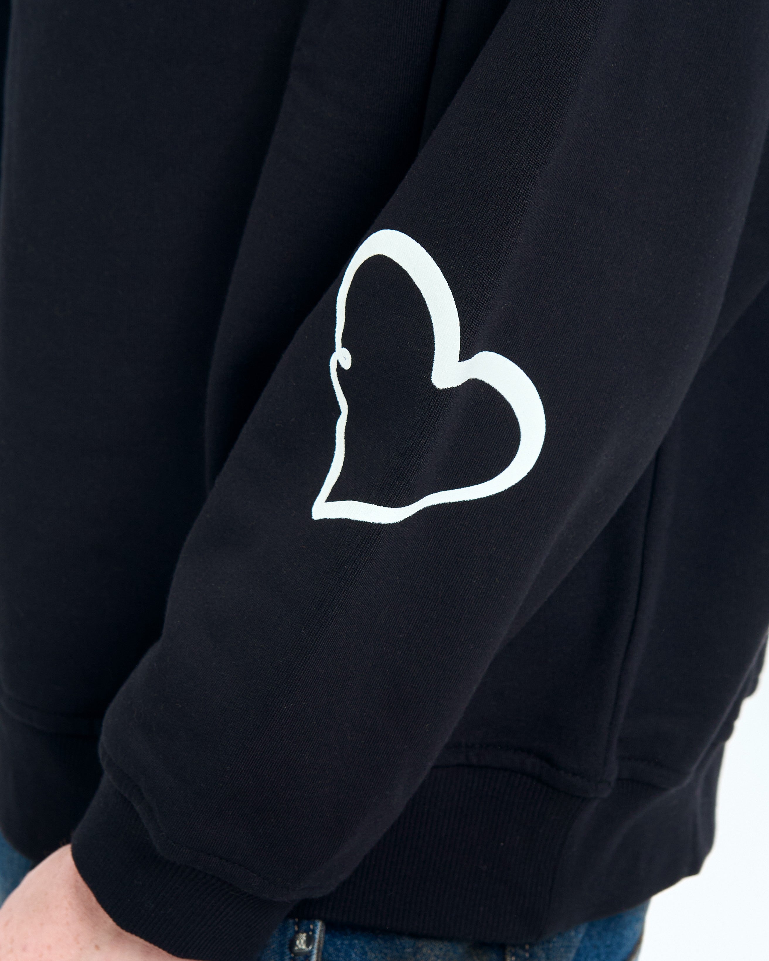 Detailaufnahme Herz-Stickerei - weisses Herz-Outline auf schwarzem Aermel des MOE CHARLIE Forbidden Sweaters