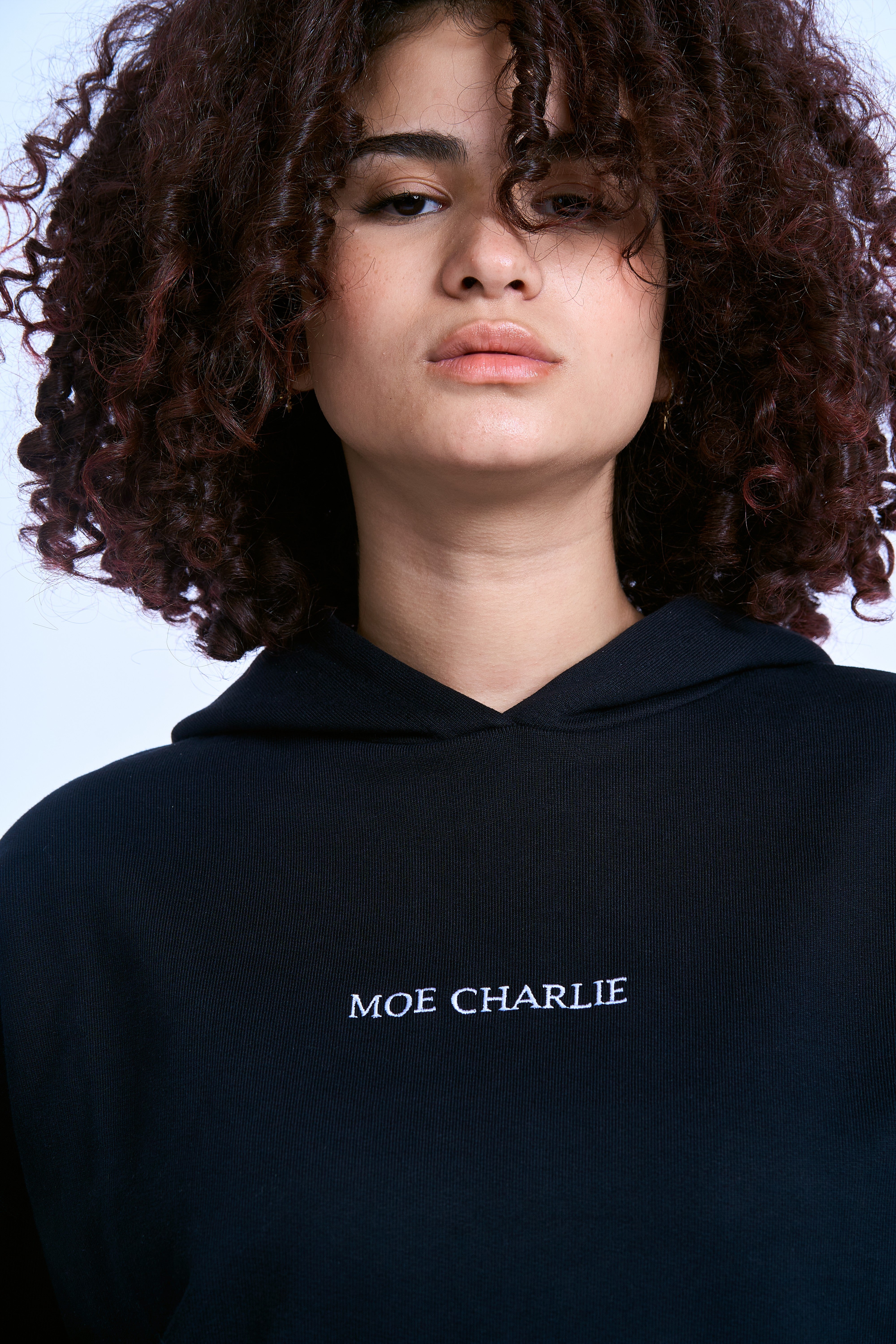 MOE CHARLIE Hoodie Schwarz, weibliche Traegerin, Nahaufnahme Brust - MOE CHARLIE Schriftstickerei, Locken