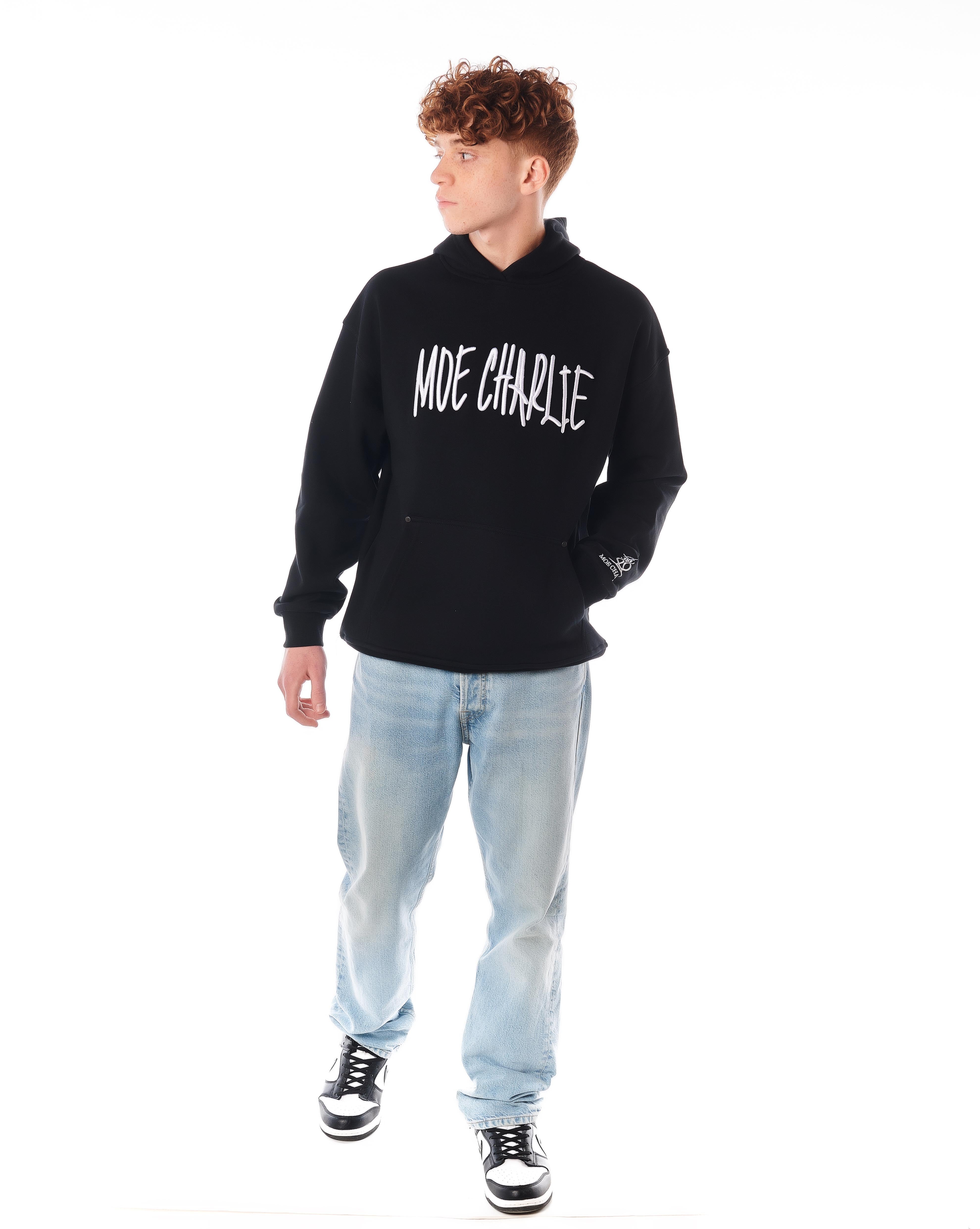 Night Life Hoodie von MOE CHARLIE, Ganzkörperpose leicht angewinkelt, Hände in Känguruh-Tasche, Jeans und Sneaker
