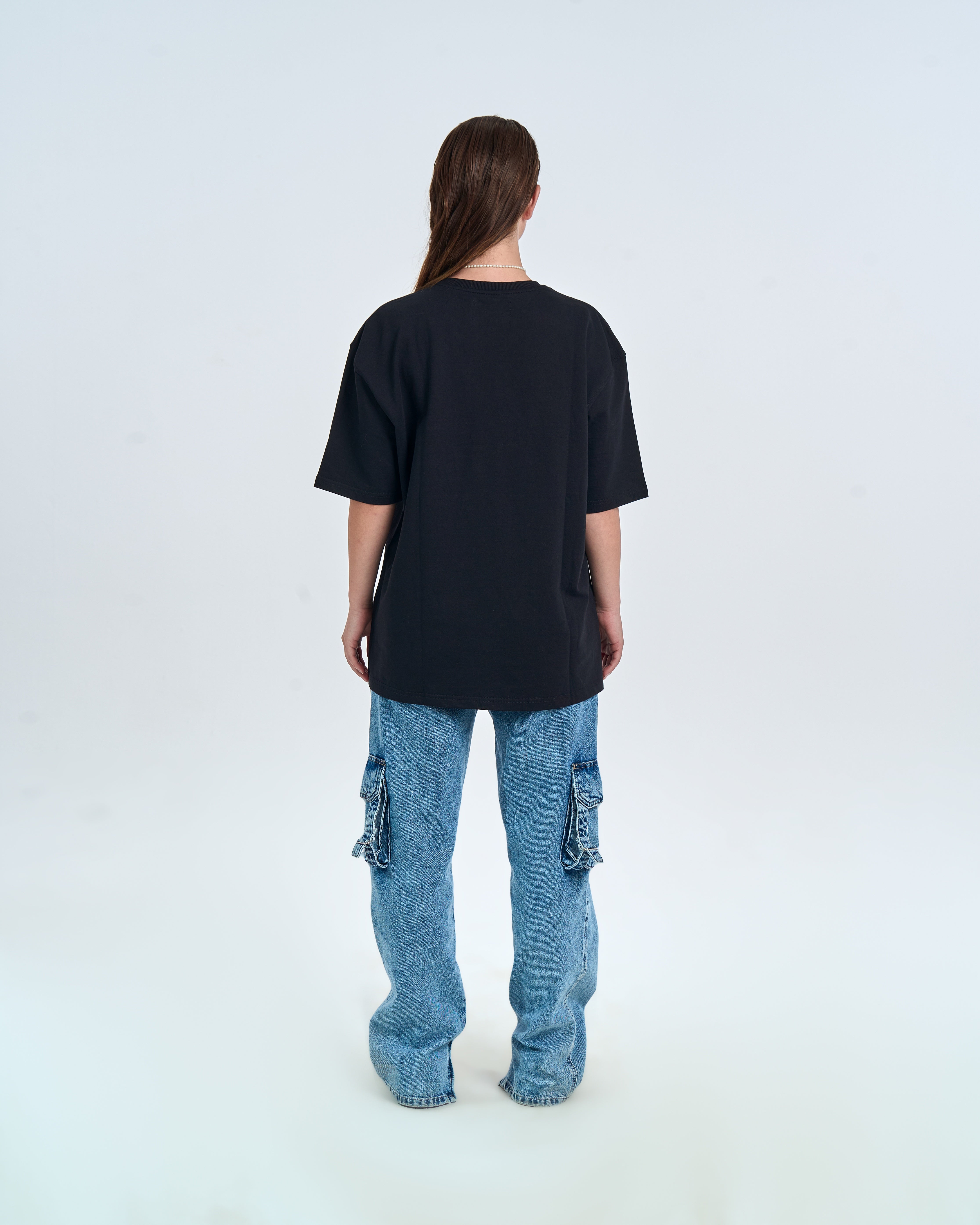 MOE CHARLIE Basic T-Shirt Schwarz – Rückenansicht Damenmodel, Oversize-Länge, hellblaue Cargo-Jeans
