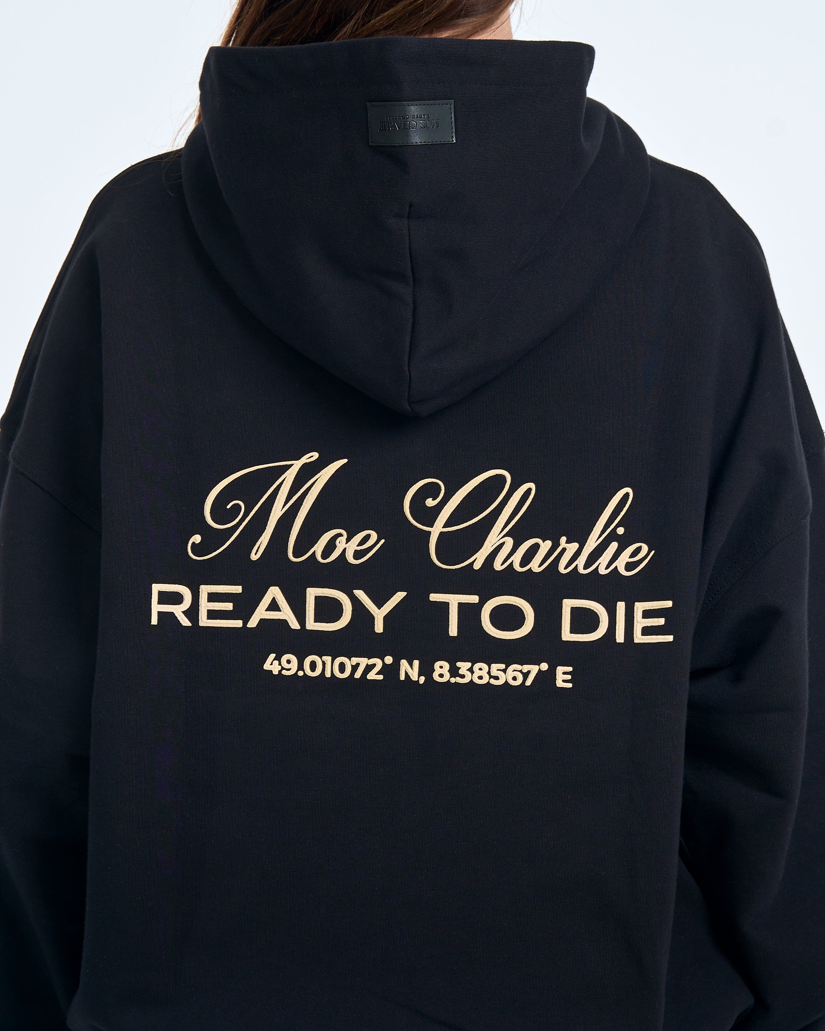 Detailaufnahme Rückendruck MOE CHARLIE Ready to Die – gold-cremefarbener Schriftzug mit GPS-Koordinaten