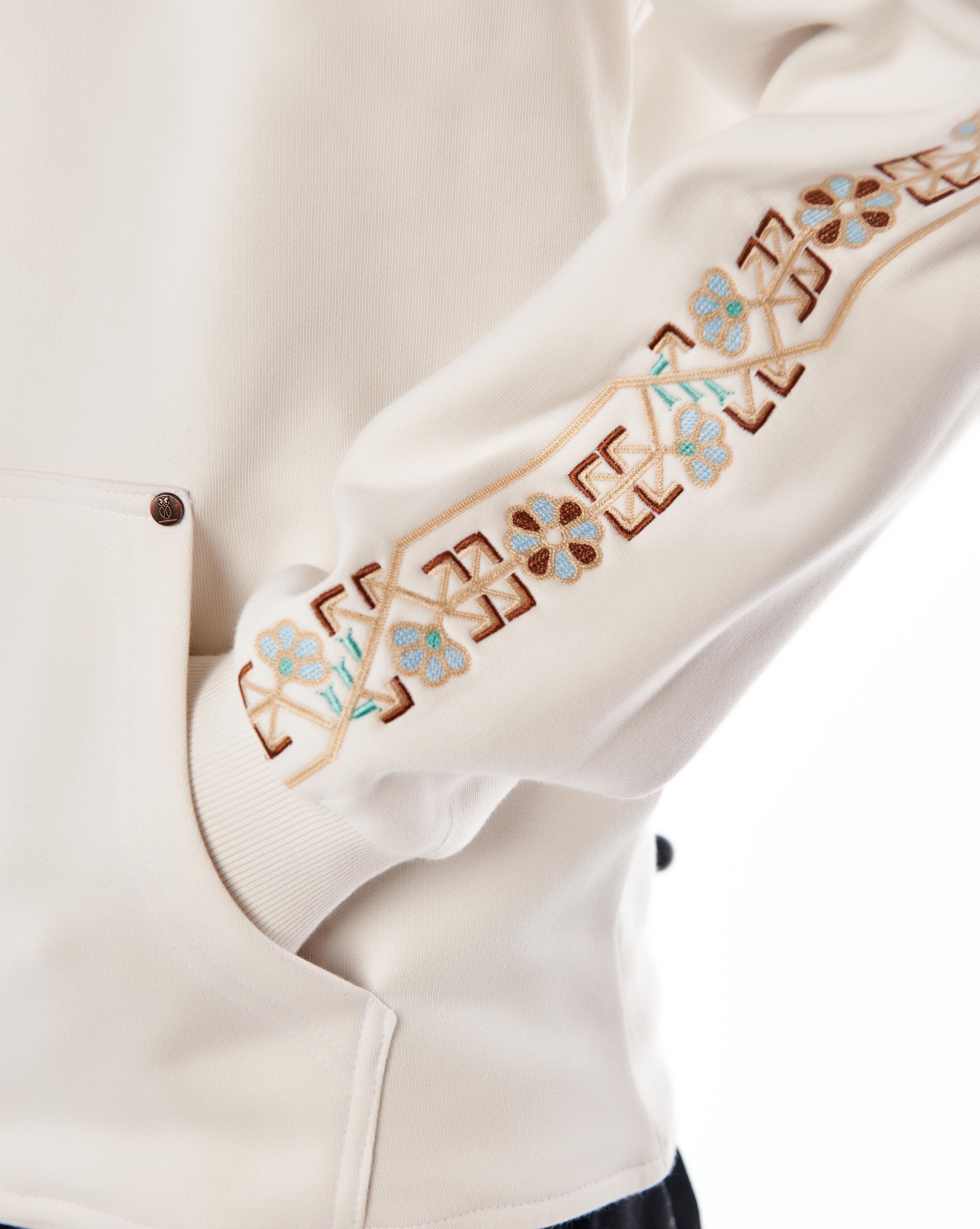Detailaufnahme der Ärmel-Stickerei am MOE CHARLIE Star White Hoodie, geometrische und florale Muster in Braun und Blau