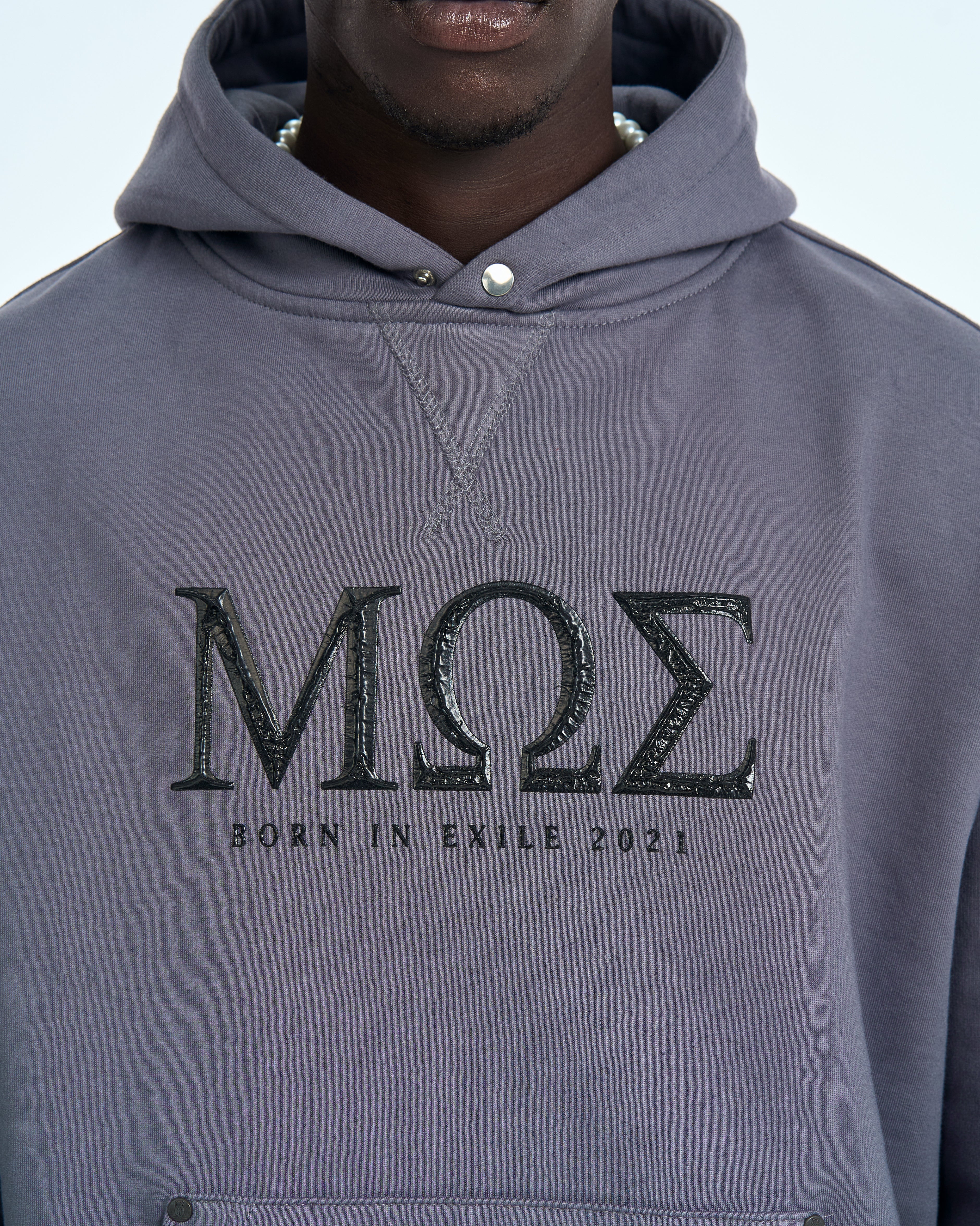 MOE CHARLIE Born in Exile Hoodie Grau, maennlicher Traeger, Nahaufnahme Front mit Perlenkette und MOE-Print