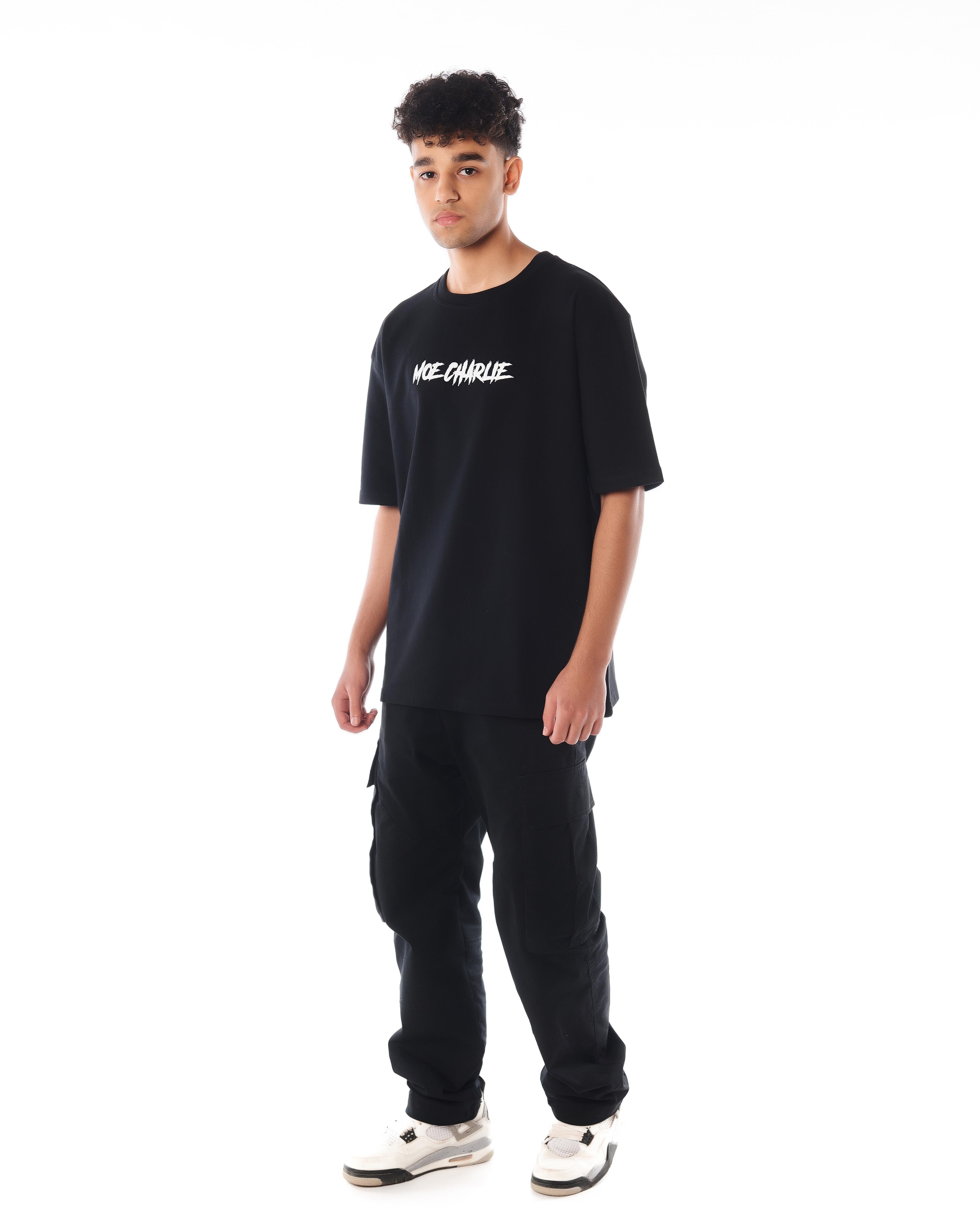 Ganzkörper-Frontansicht MOE CHARLIE Predator T-Shirt, schwarze Cargo-Kombination, weiße Sneakers