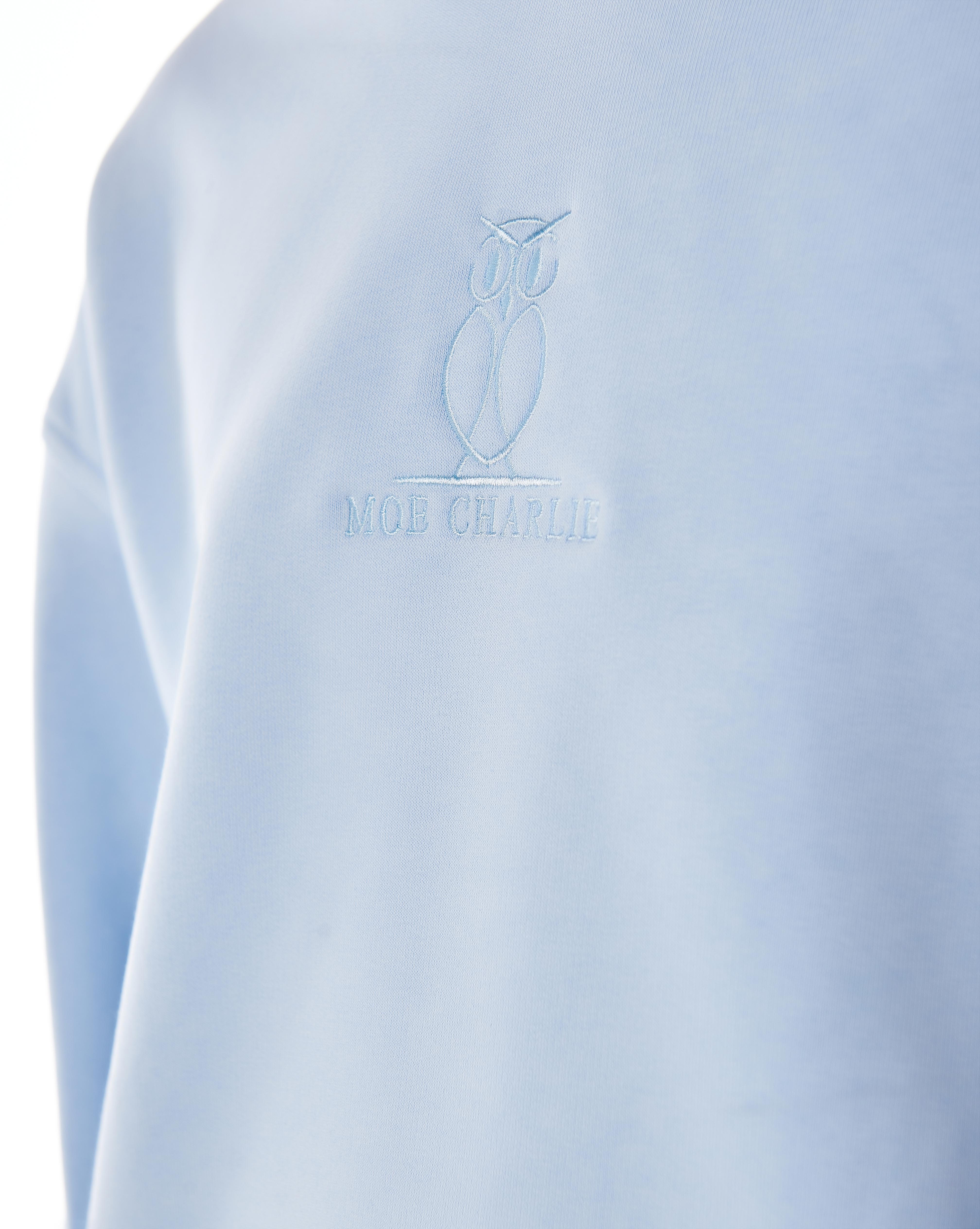 Detailaufnahme des ton-in-ton gestickten MOE CHARLIE Owl-Logos auf der linken Brust des Riviera Blue Hoodies