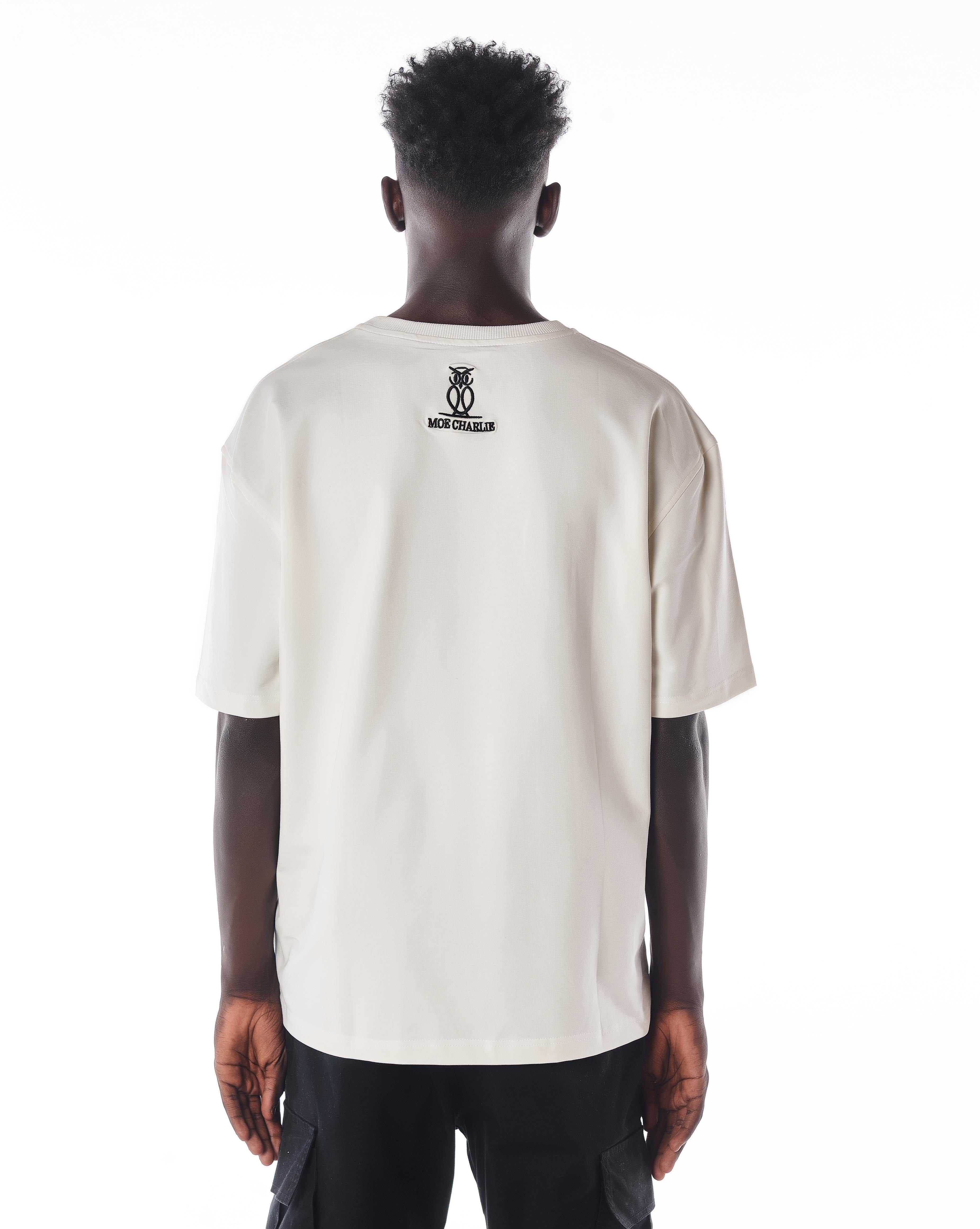 Rückenansicht MOE CHARLIE Gold Passion T-Shirt, schwarzes Eulen-Logo am Nacken auf cremefarbenem Stoff
