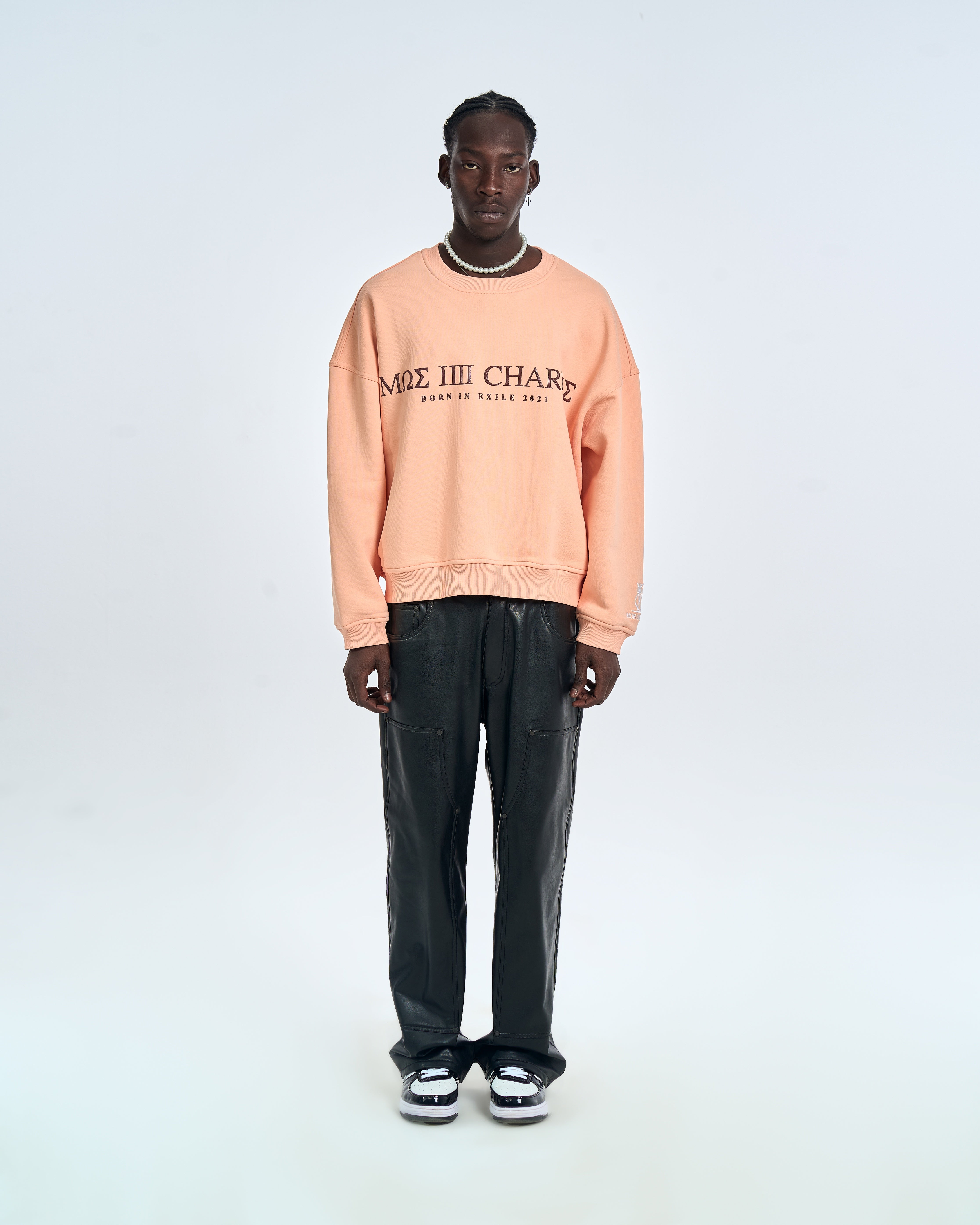 MOE CHARLIE Born In Exile Sweater Peach – Frontansicht Herrenmodel, dunkler MΩΣ-Frontprint, schwarze Lederhose