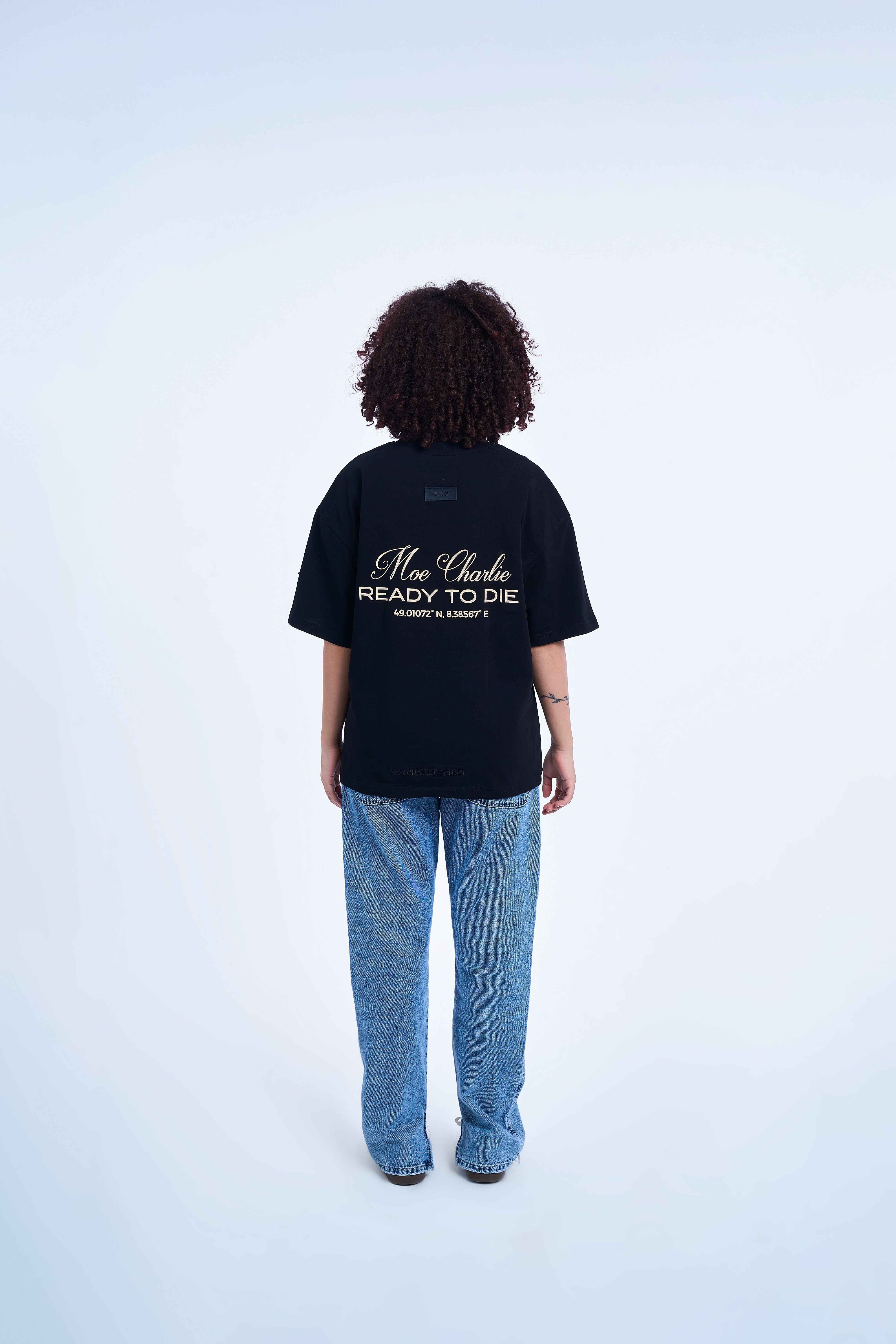Rückenansicht weibliches Model MOE CHARLIE Ready To Die Shirt – cremefarbener Backprint, hellblaue Flare Jeans